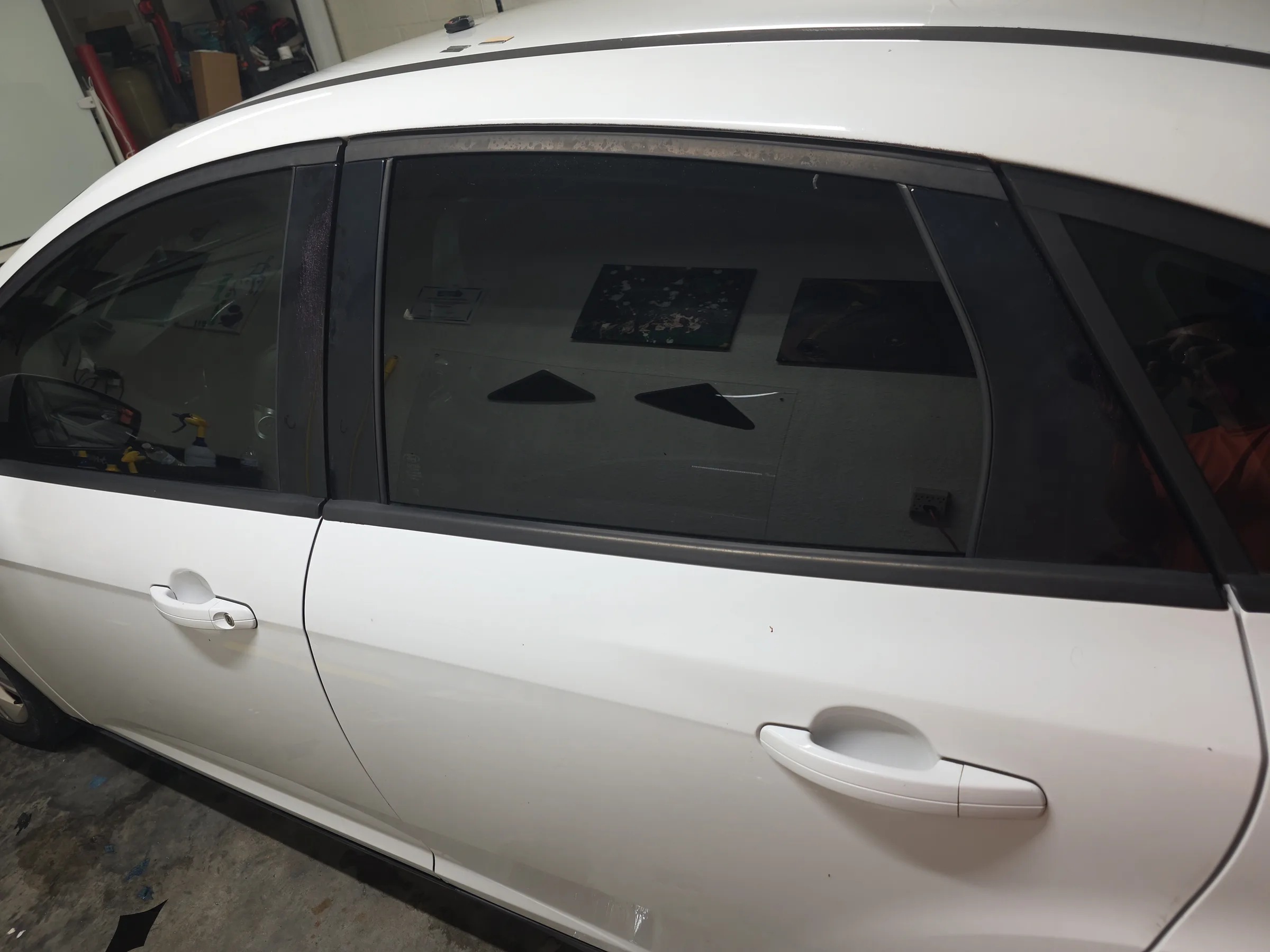 White SUV with dark window tint applied to the side windows during installation at an indoor workshop.