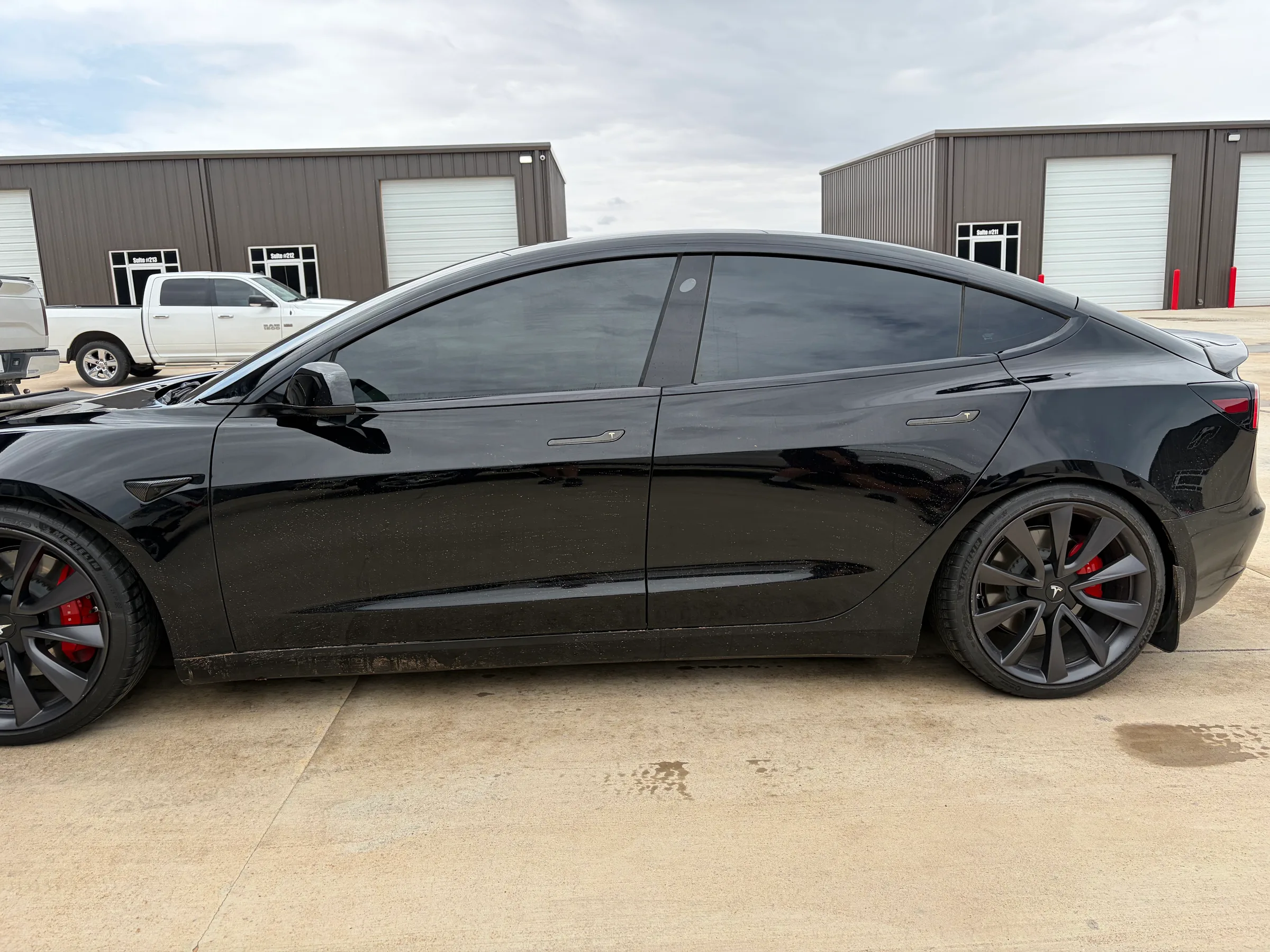 Black Tesla Model S with dark window tint applied, shown from the driver's side at a commercial facility.