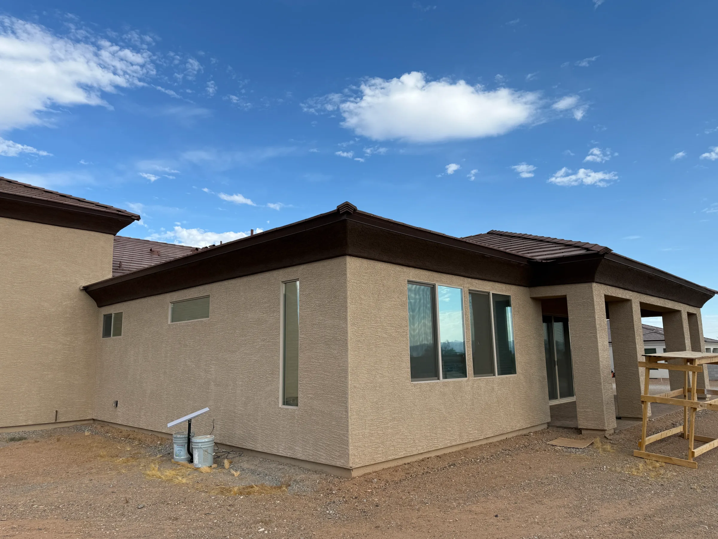 A tan brick residential home with large windows and dark-tinted window film applied to the exterior windows, photographed under clear Arizona sky.
