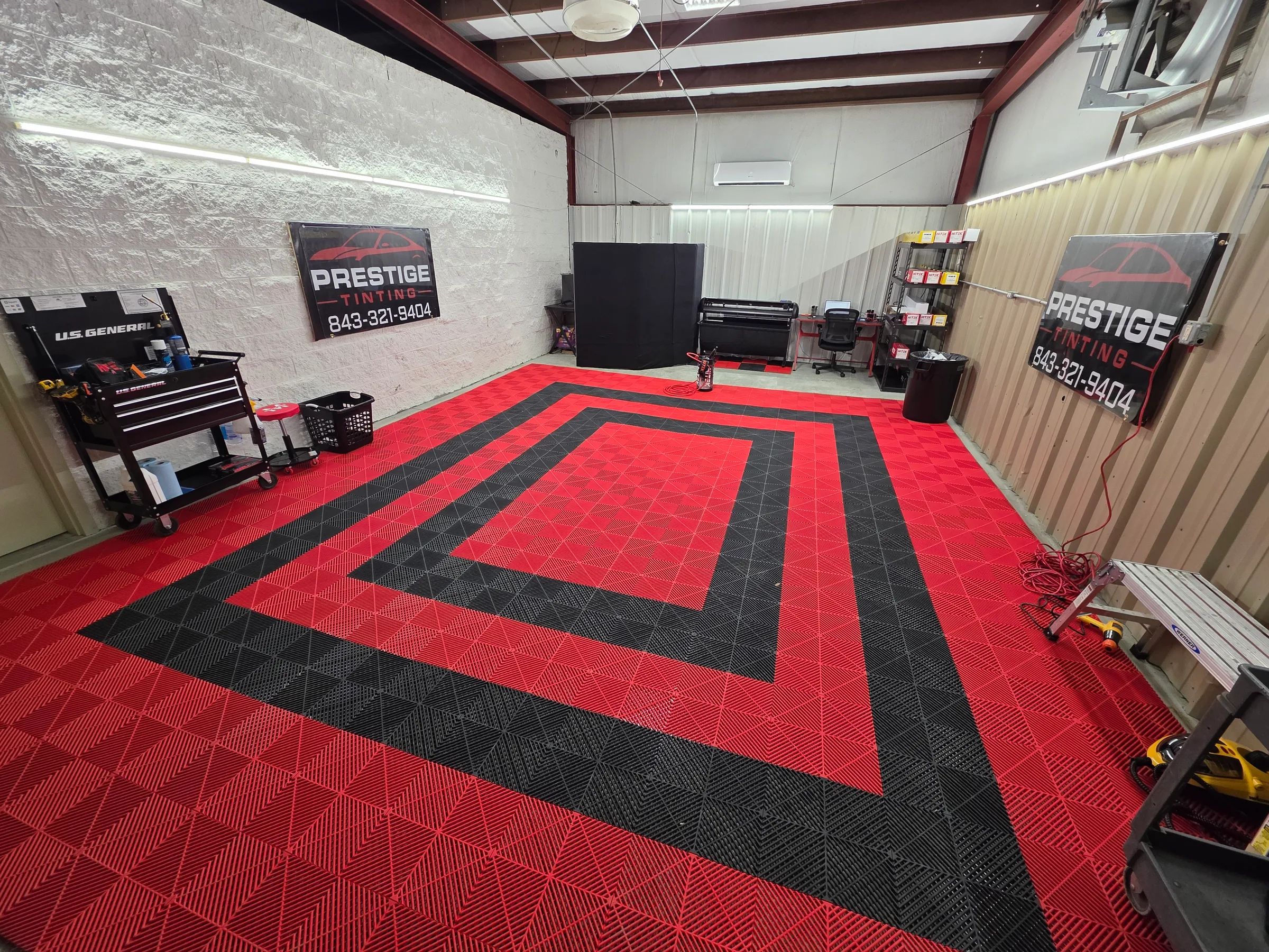 Interior of Prestige Tinting LLC's workshop in Conway, SC featuring a red and black geometric floor design, workbenches, and branded signage.