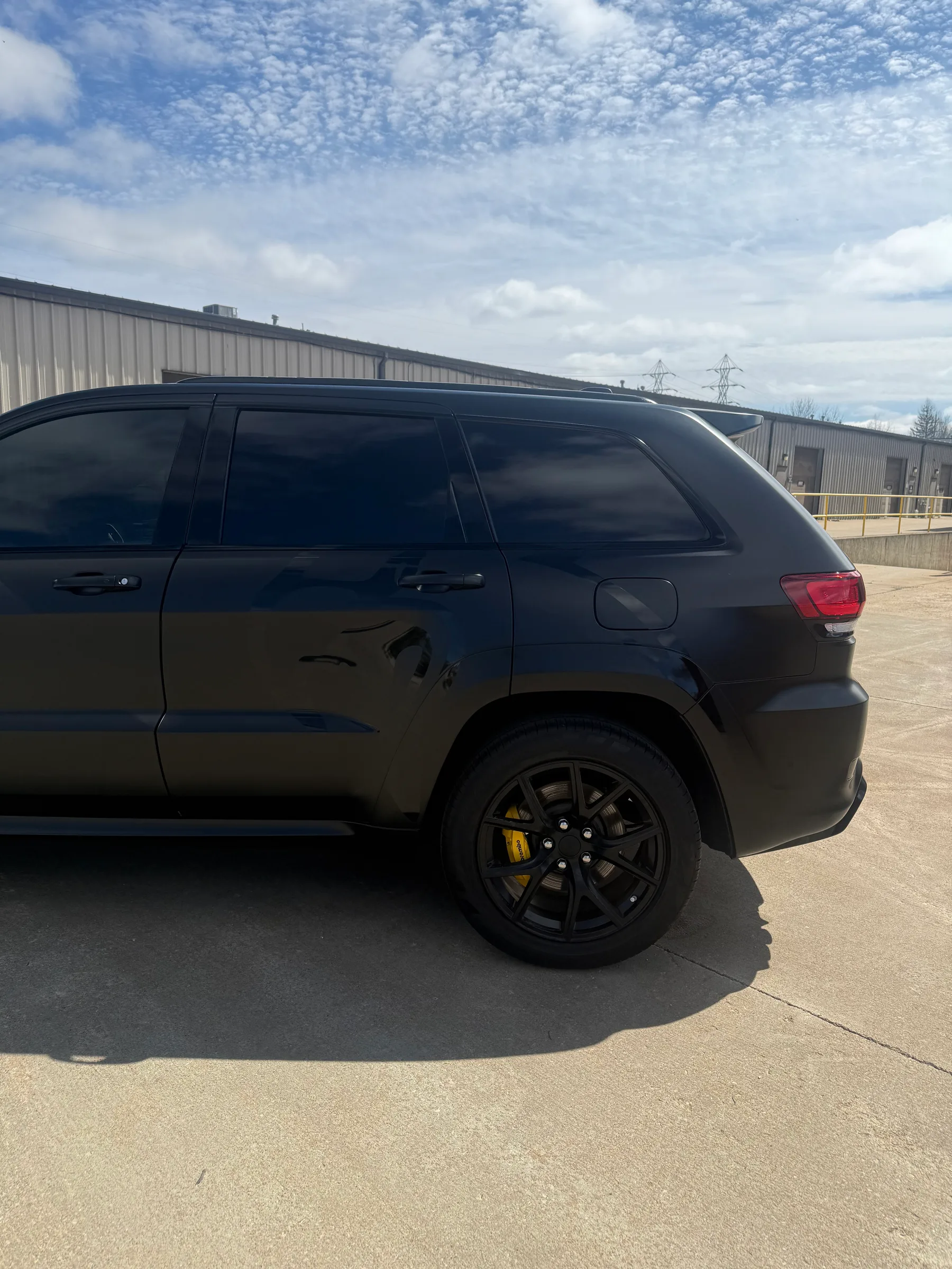 A black SUV with dark tinted windows parked in a lot outside an industrial building.