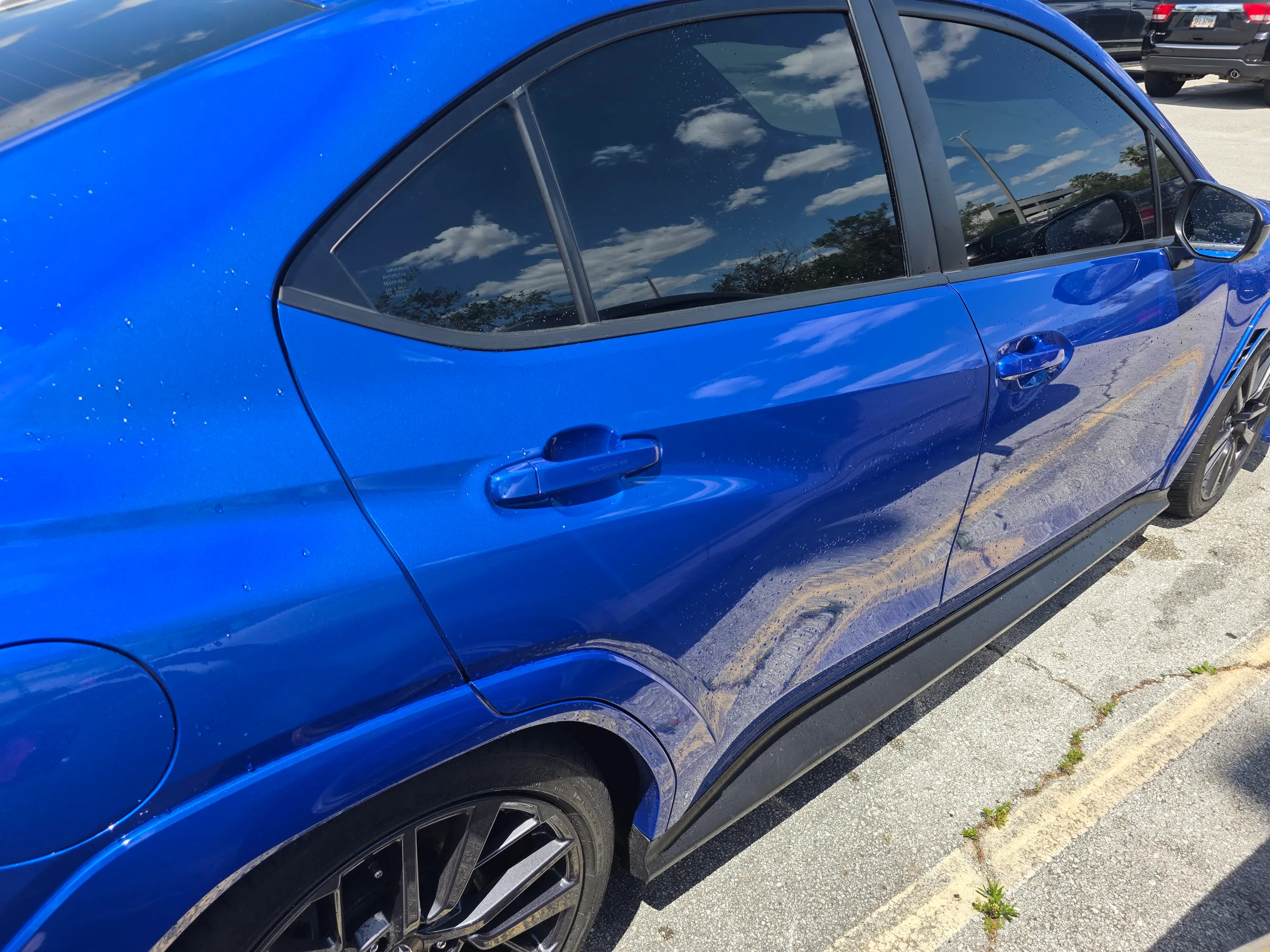 A bright blue car with darkly tinted windows parked in a lot, showing professional window tinting applied to the side and rear glass.