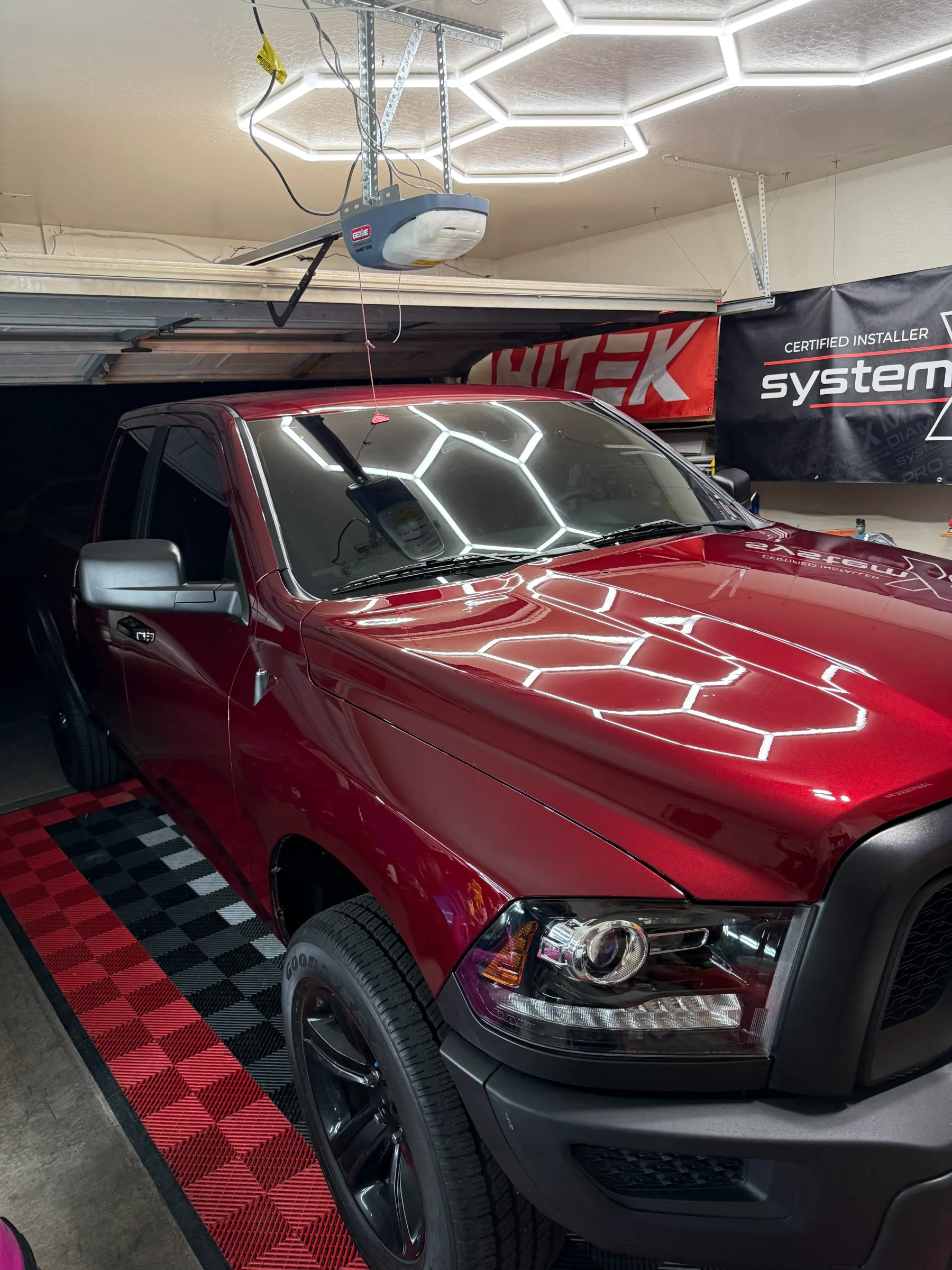 A red Ram pickup truck with a freshly applied ceramic coating displayed in a professional shop bay, showing the glossy finish and hydrophobic beading pattern on the hood and windshield.