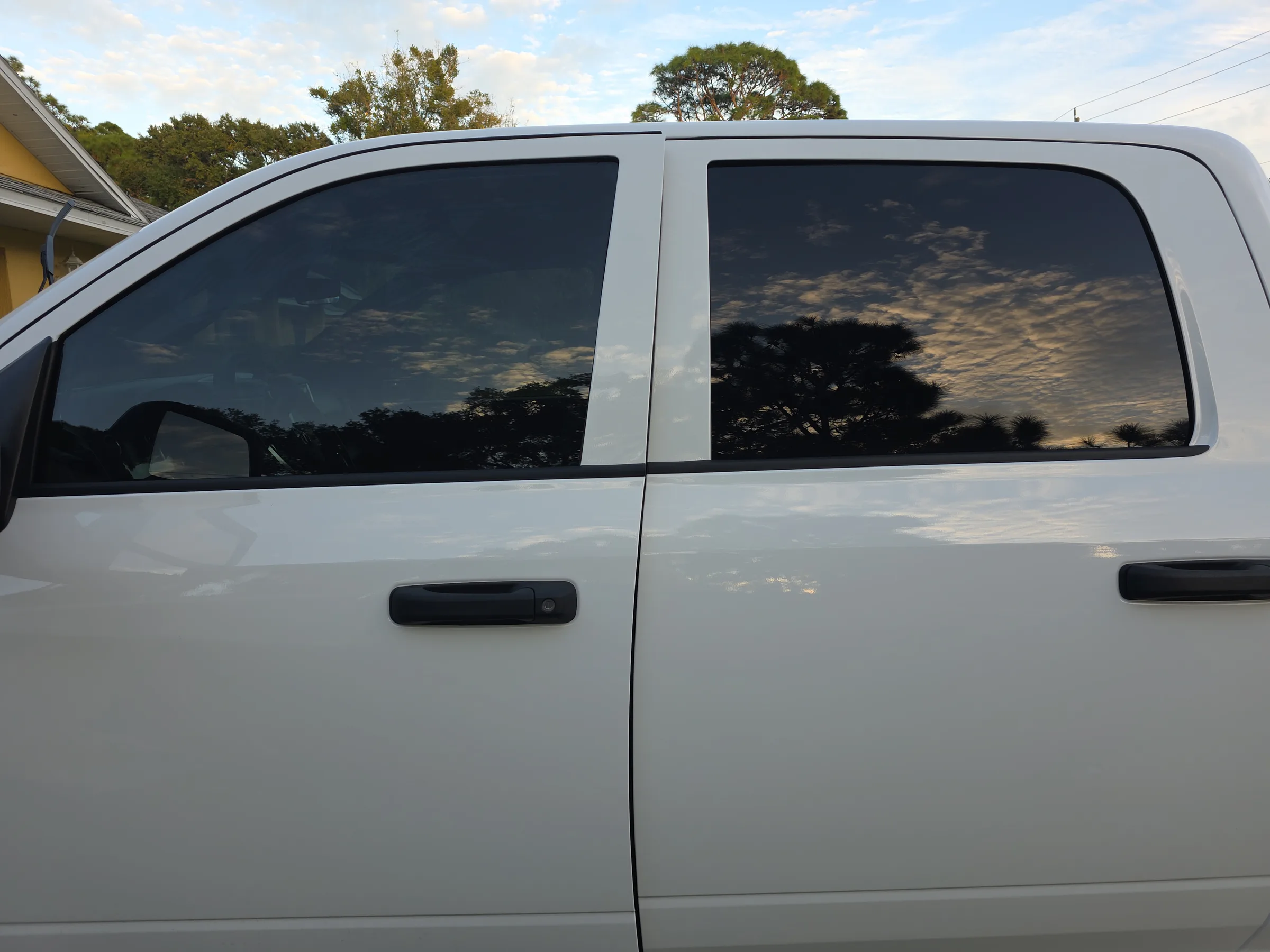 White van with dark window tint applied to the rear passenger windows, showing the reflective tint finish against a cloudy sky and trees.