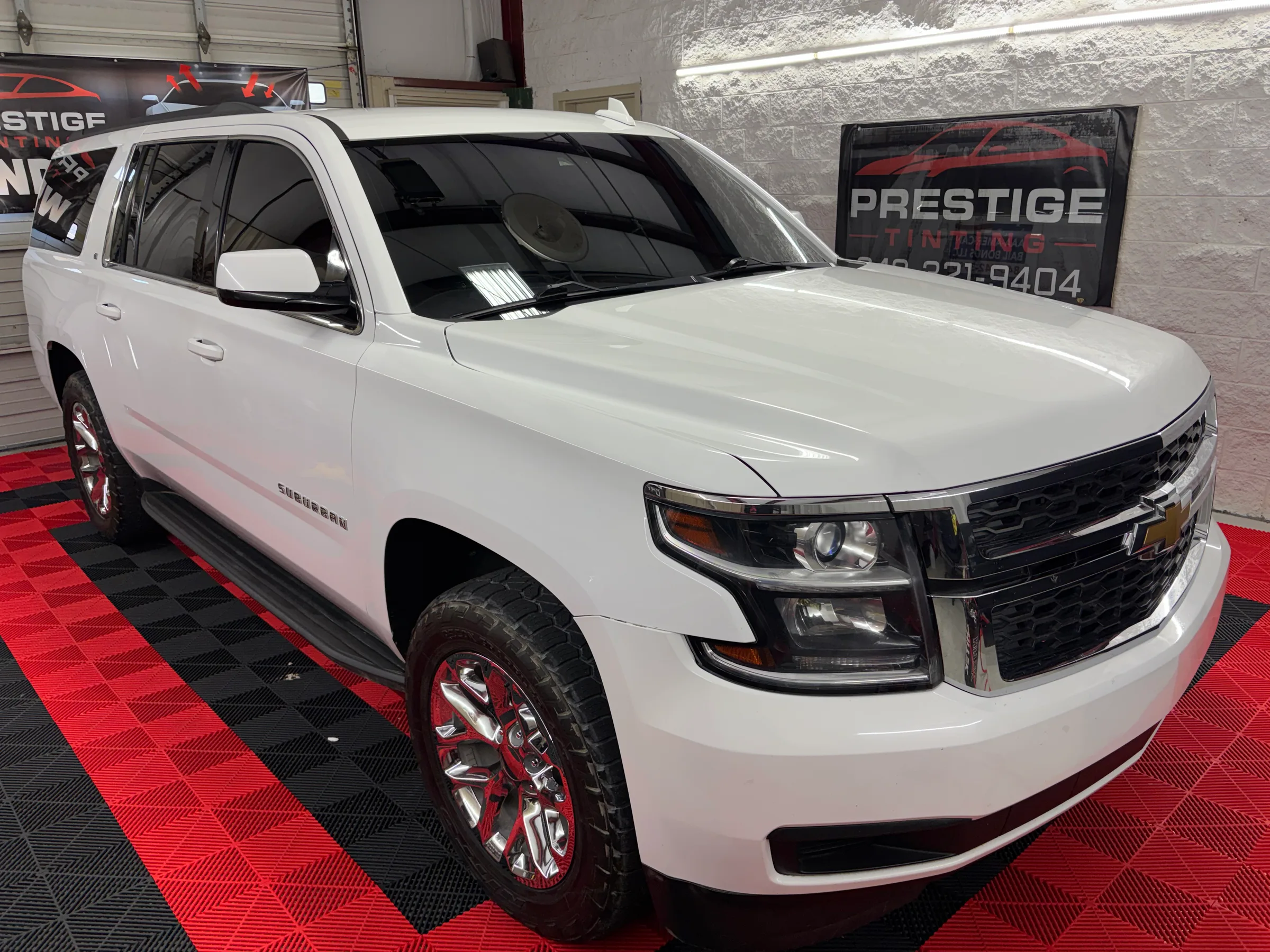 White Chevrolet Suburban with dark window tint displayed in a shop showroom with a Prestige Tinting sign visible in the background.