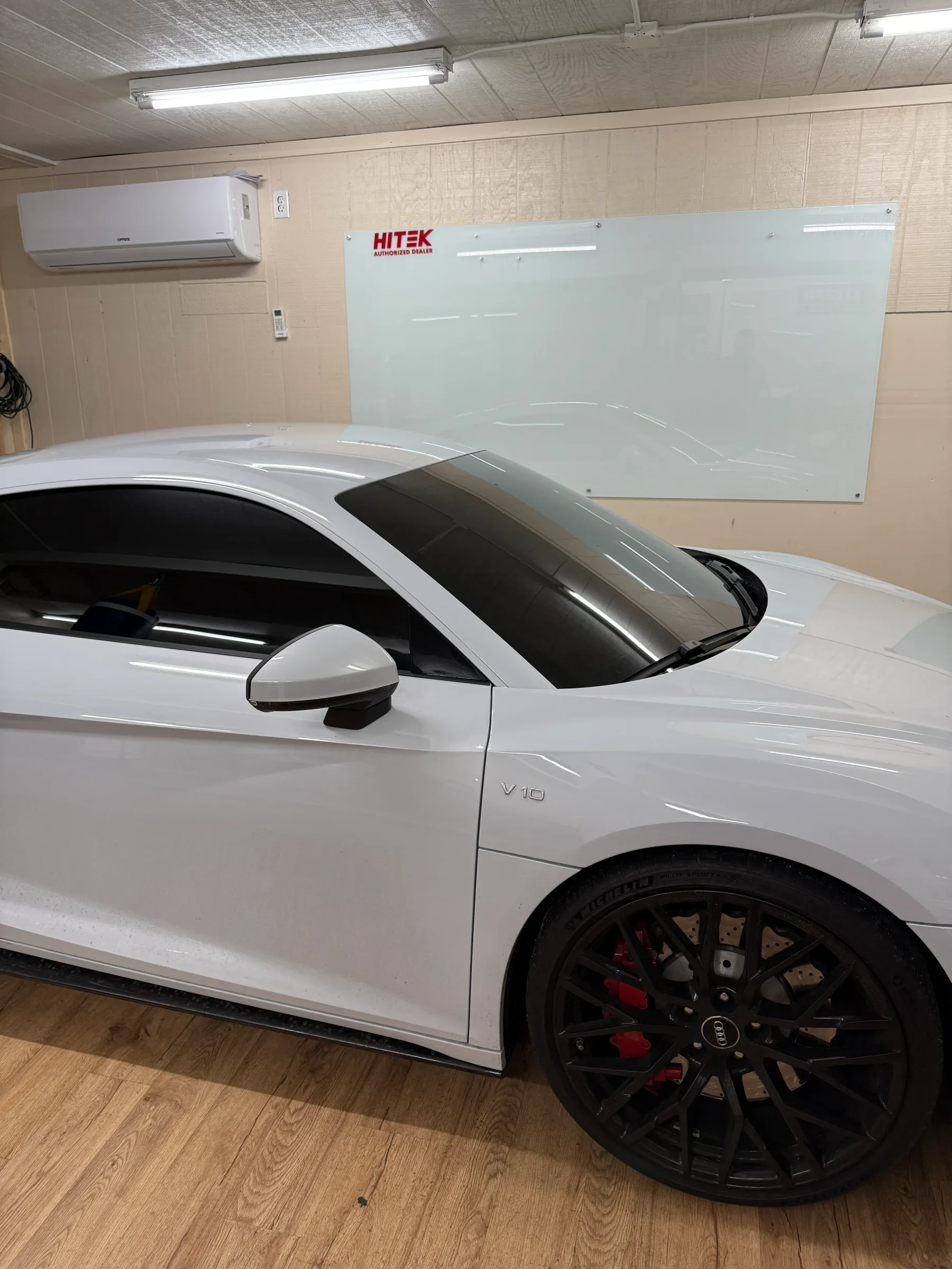White BMW i4 with window tint applied, parked in an indoor service bay with HITEK branding visible on the wall.
