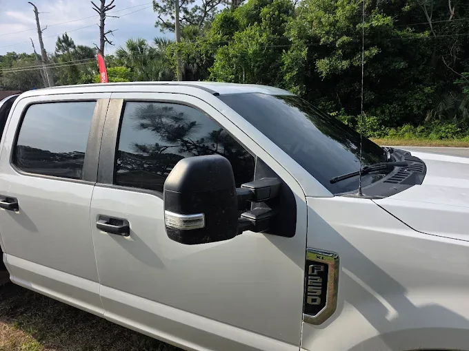 A white pickup truck with dark window tint applied to the side and rear windows, parked outdoors with trees in the background.