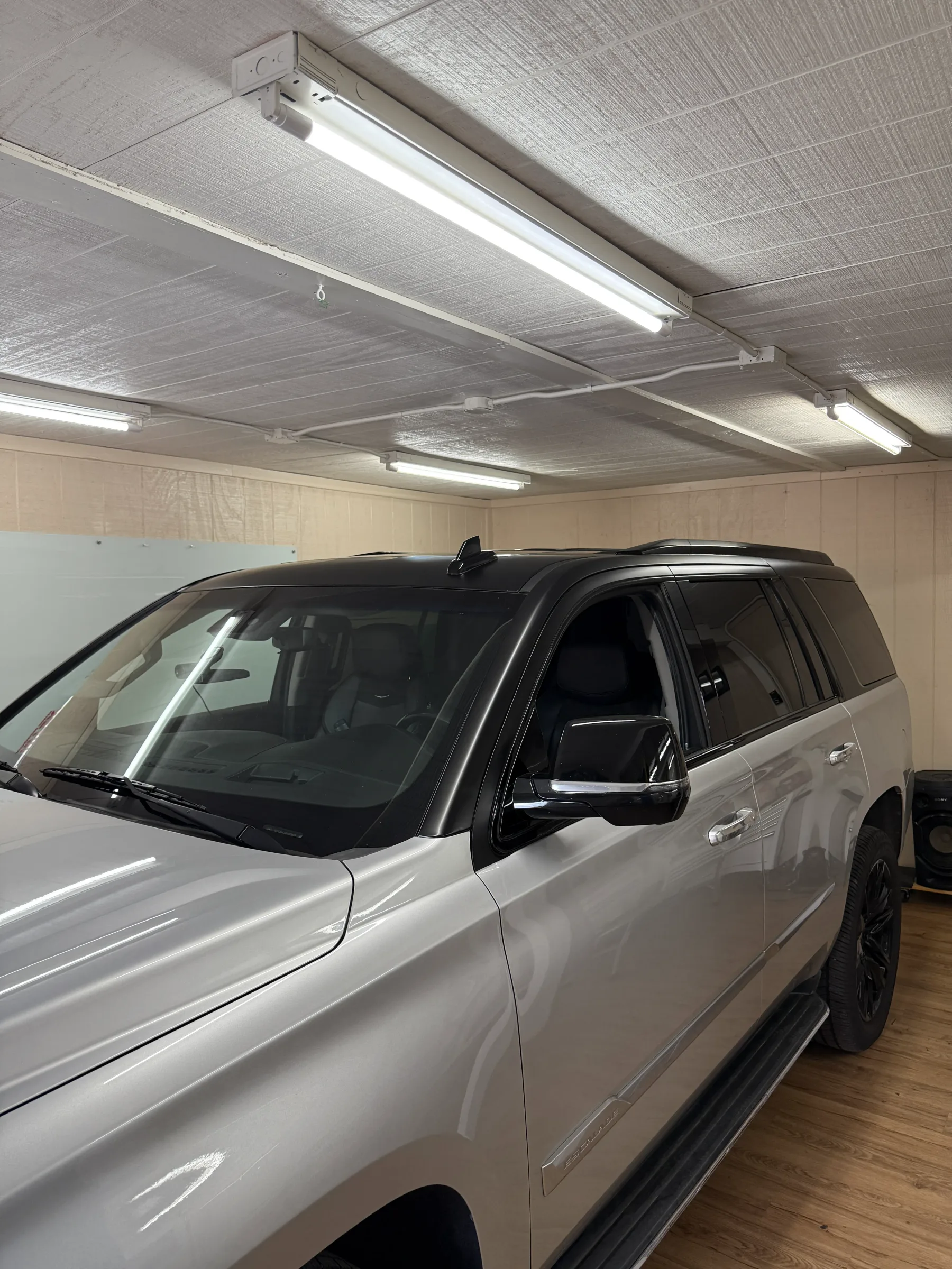 A silver SUV with dark window tint applied to all side windows, parked in an indoor service bay with fluorescent lighting.