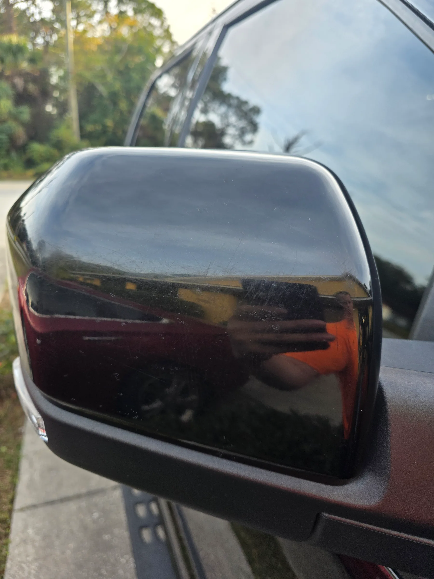 Close-up of a vehicle side mirror with dark window tint applied, reflecting trees and sky.