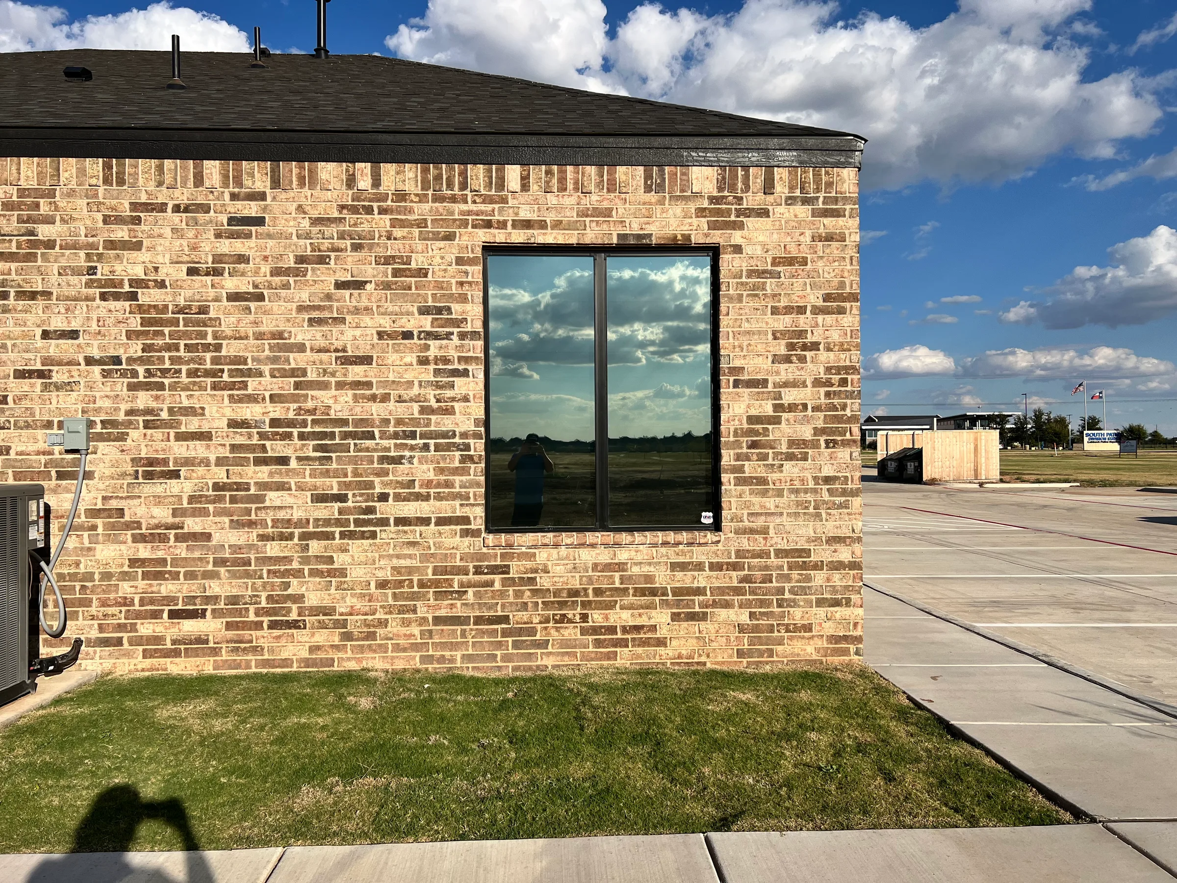 A brick commercial building with large tinted windows reflecting the sky, showcasing window film installation on a residential property.