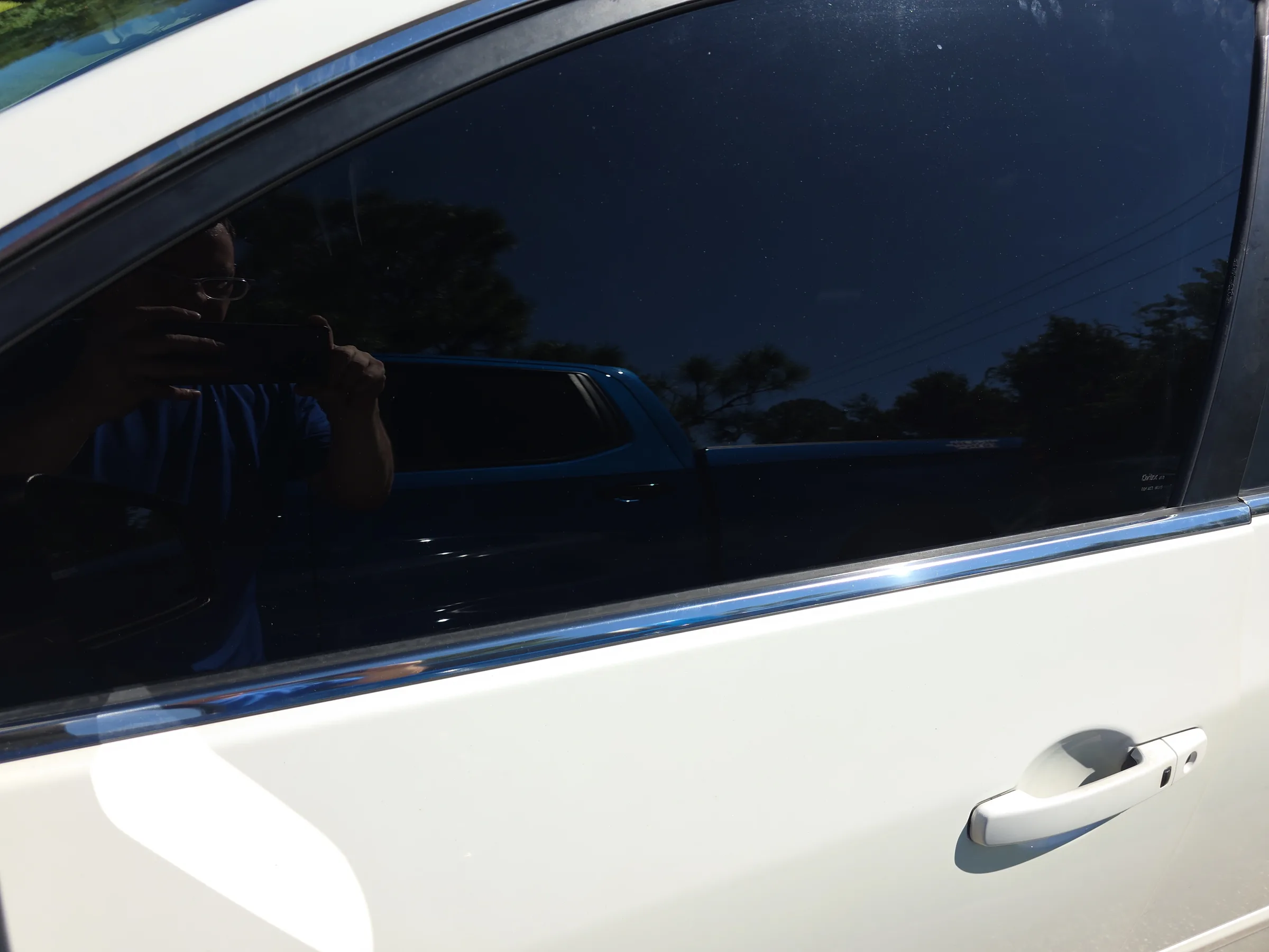 Close-up view of a white SUV's rear window with dark window tint applied, showing the contrast between the tinted glass and white door panel.