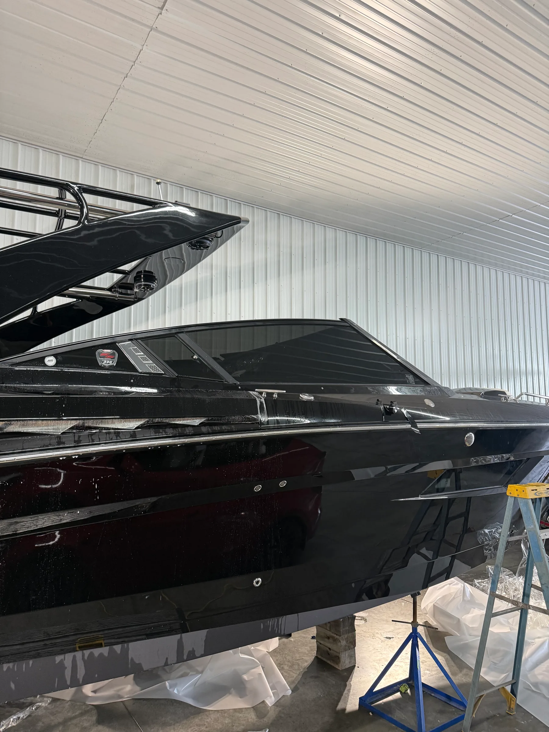 Multiple black boats in an indoor facility undergoing protective film application and wrapping work.