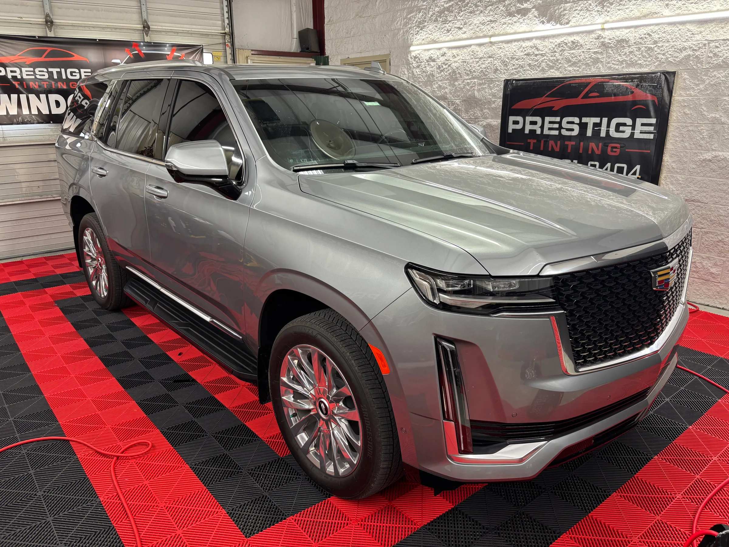 Silver Cadillac XT6 SUV with tinted windows displayed in a showroom with red and black floor mat, Prestige Tinting signage visible in the background.