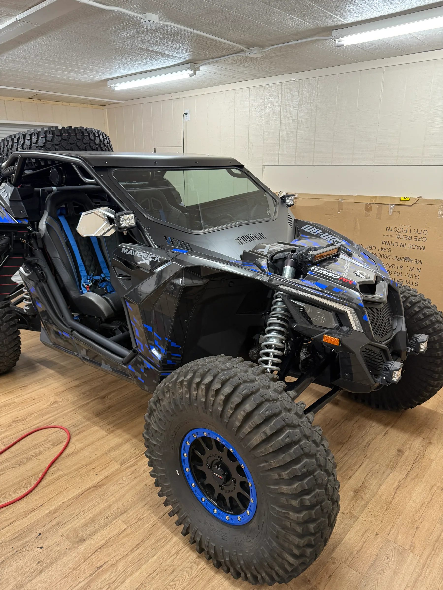A black and blue Can-Am Maverick off-road UTV with tinted windows parked in an indoor workshop during window film installation.