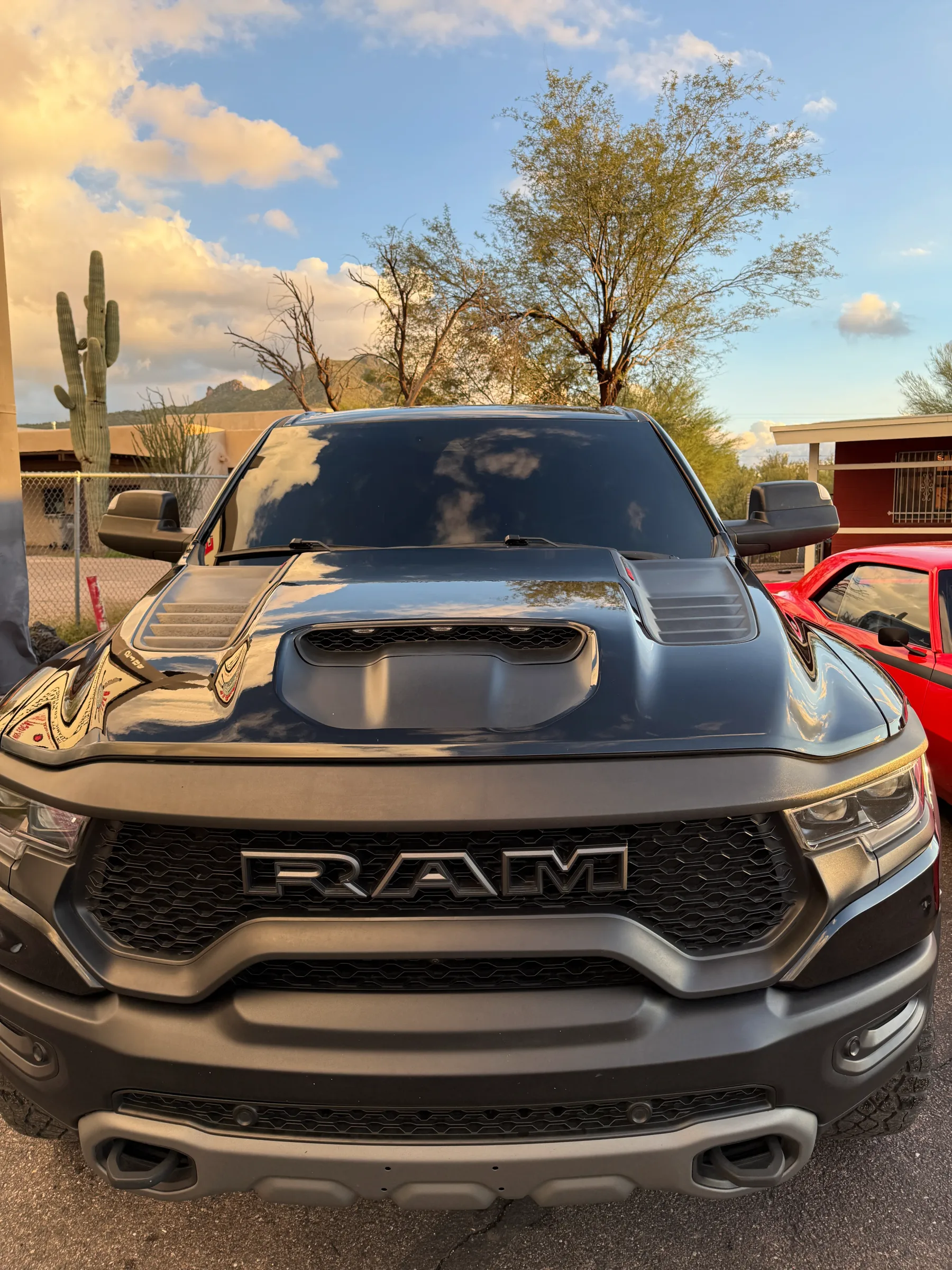 A black Dodge Ram truck with dark window tint parked in a desert shop lot with saguaro cactus and mountains in the background.