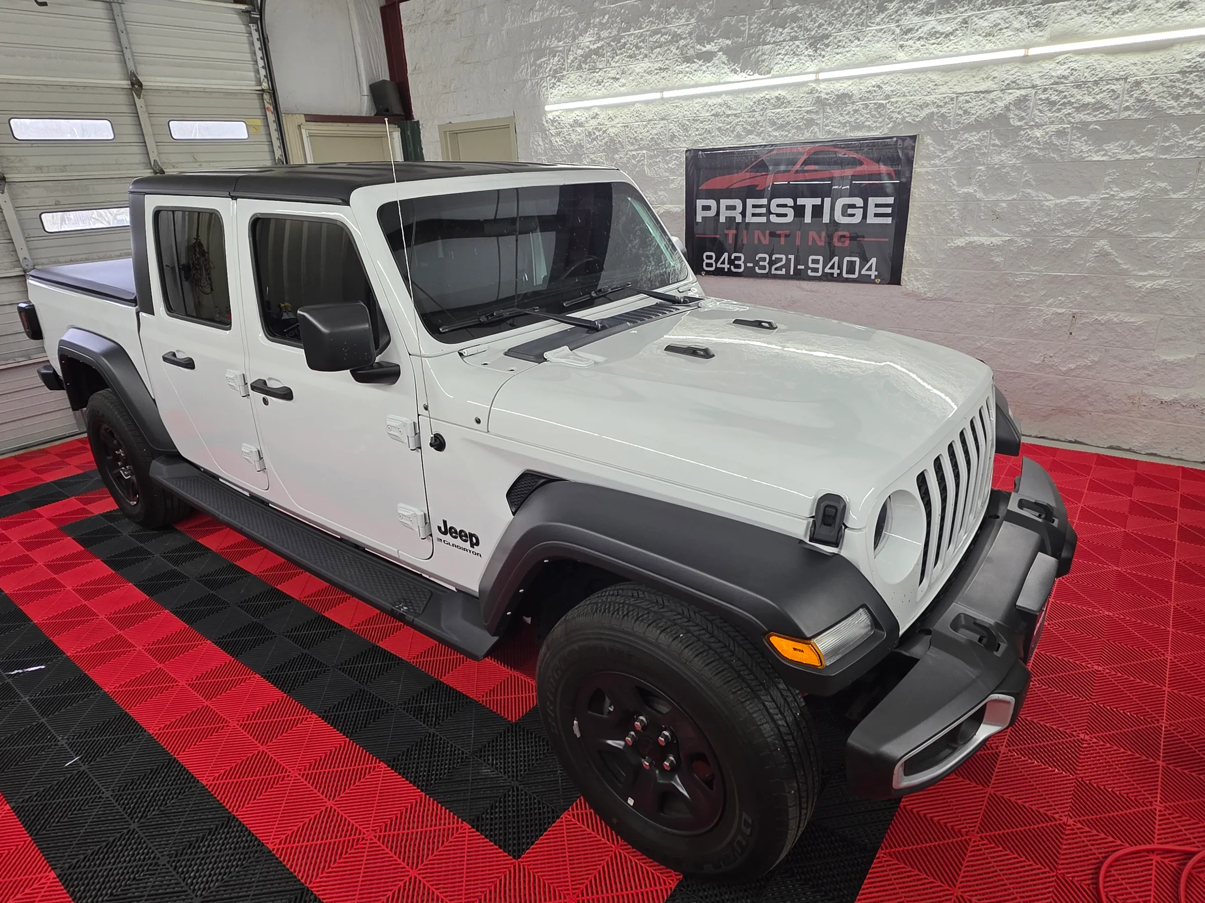 White Jeep Gladiator pickup truck with dark window tint displayed in a shop bay next to a Prestige Tinting sign.