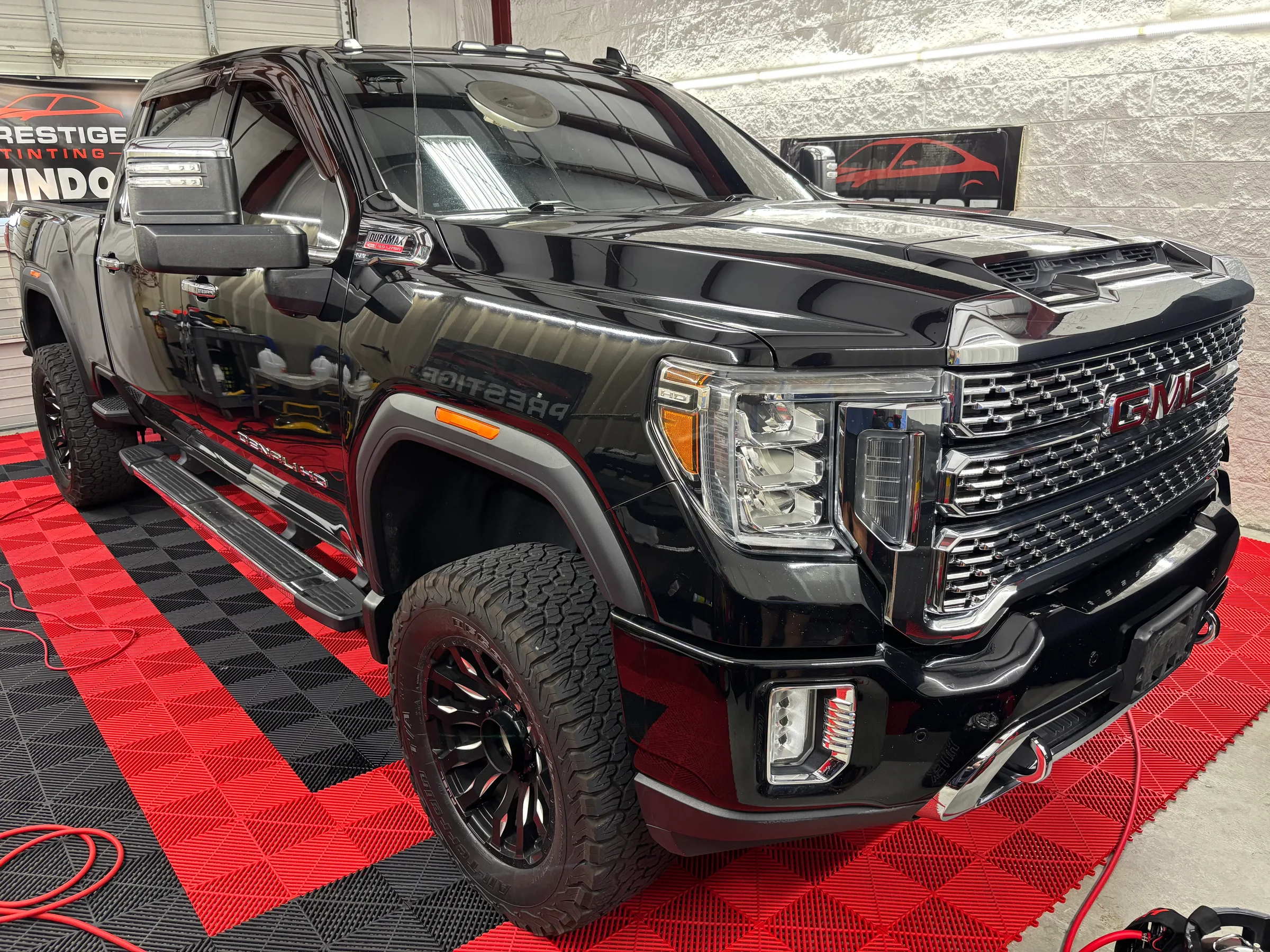 A black GMC Sierra truck with tinted windows displayed in a showroom with red and black floor mats at Prestige Tinting in Conway, SC.