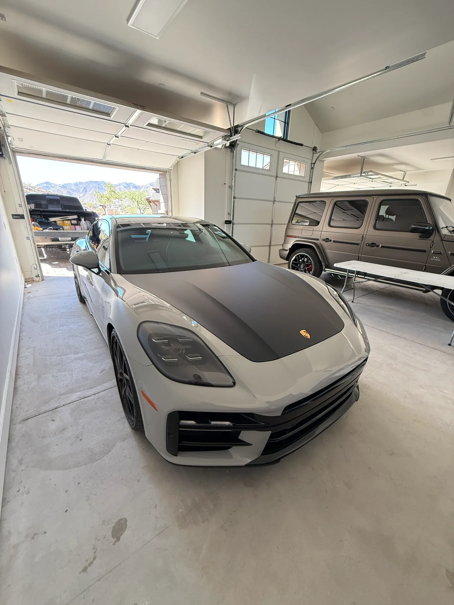 White Porsche with black headlight protection film applied, parked in a garage with mountain views in the background.