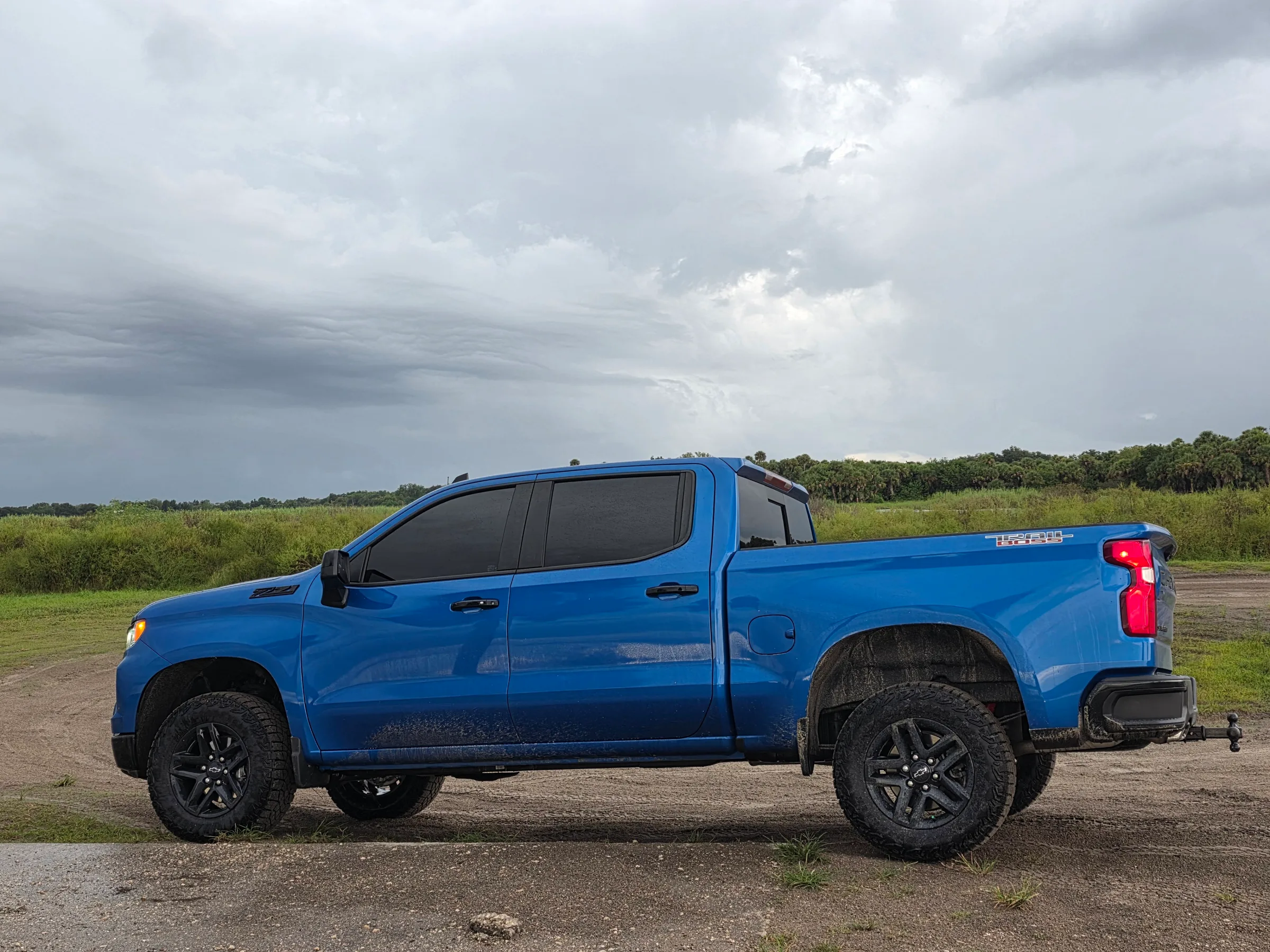 A blue Chevrolet Silverado pickup truck with dark window tint applied to all side windows, parked in an open field under cloudy skies.