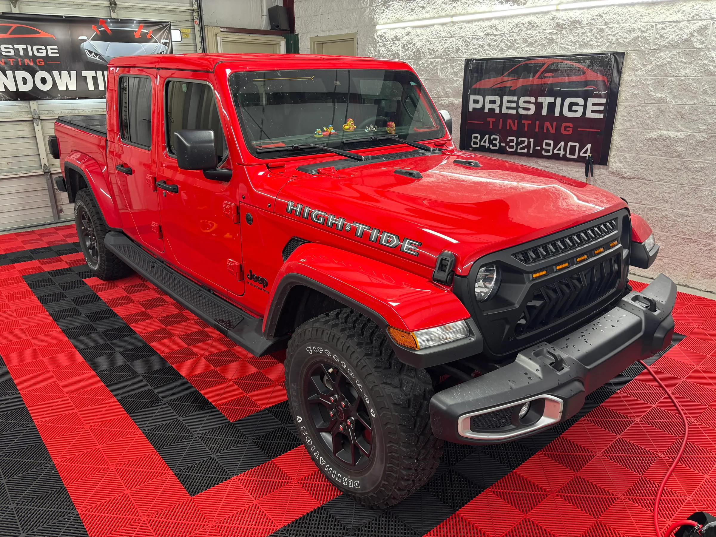 A bright red Jeep Hightide with tinted windows displayed in a showroom next to a Prestige Tinting sign.