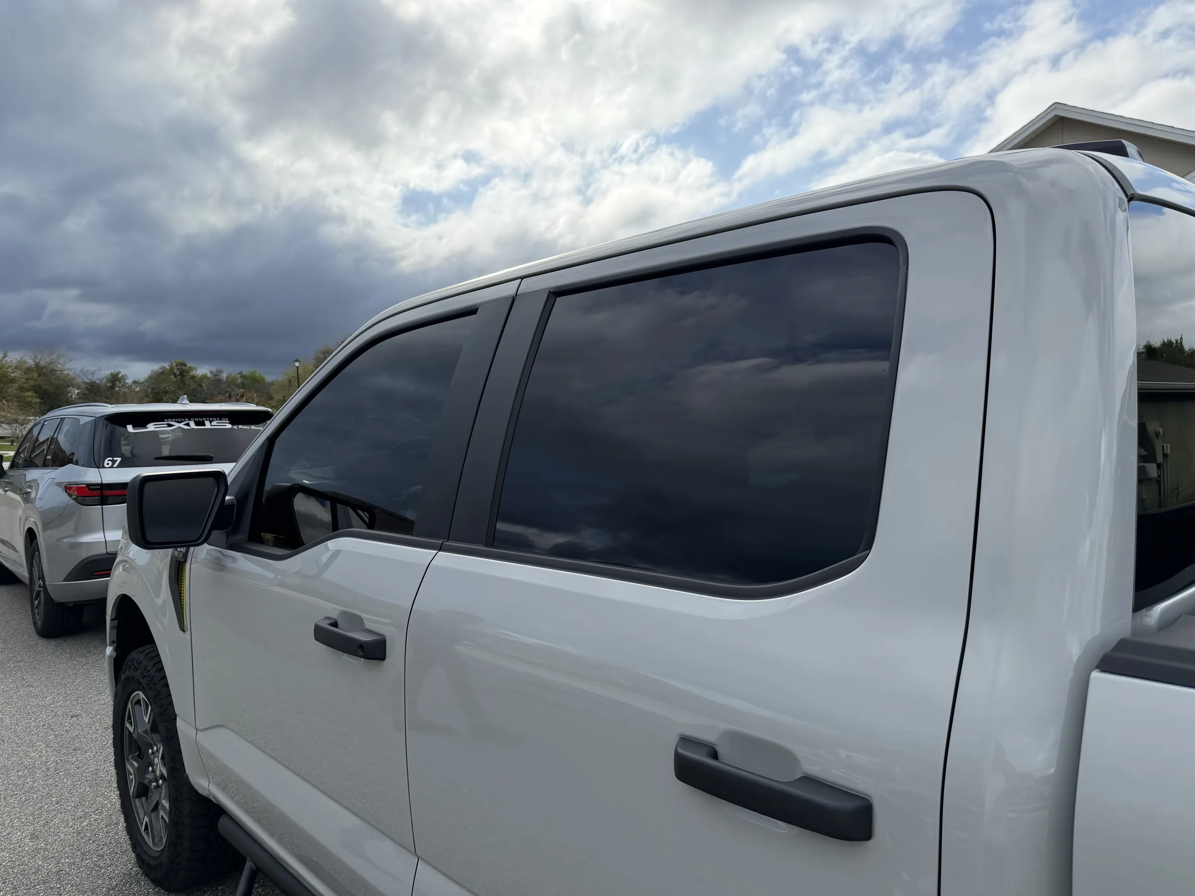 A white SUV with dark window tint applied to the side windows, parked outdoors with other vehicles visible in the background.