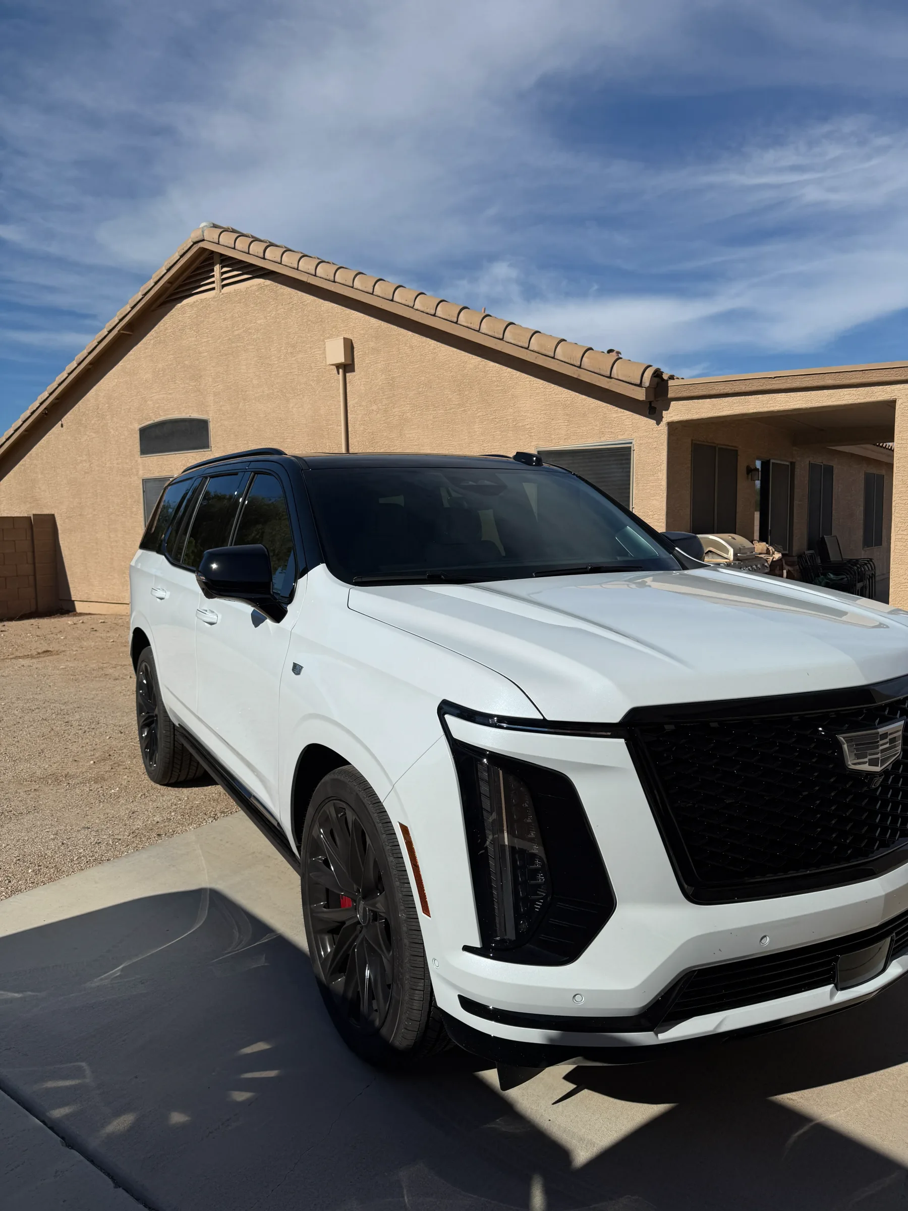 A white Cadillac SUV with dark window tint parked in front of a tan stucco building under a clear Arizona sky.