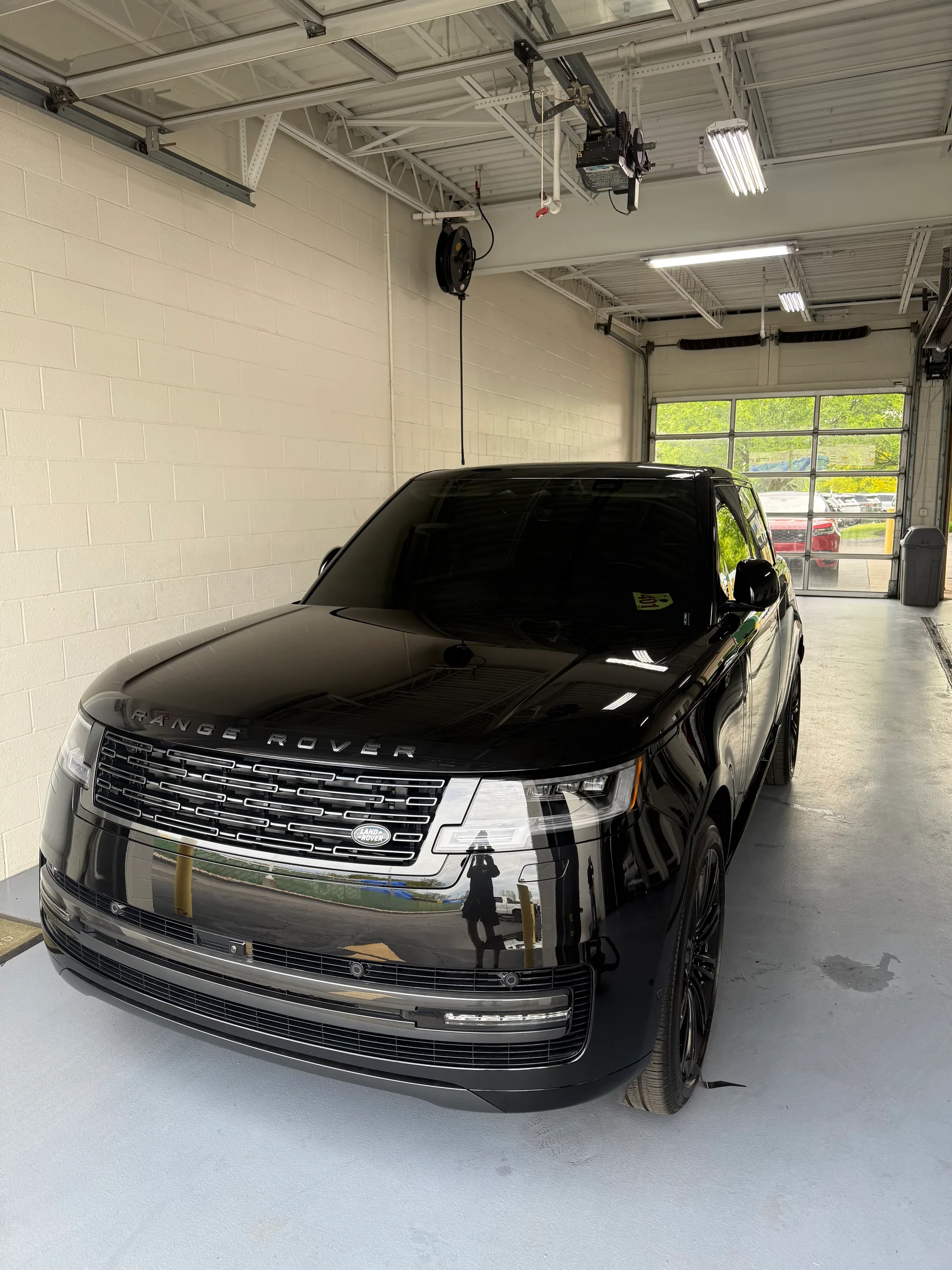 A black Range Rover SUV parked inside a professional detailing bay with white walls and overhead lighting, ready for paint protection film application.