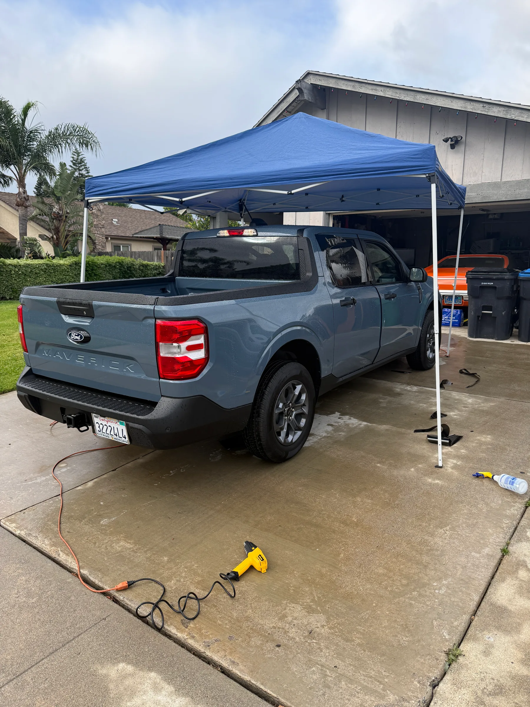 A light blue Ford Maverick pickup truck parked under a blue canopy tent during window tinting service.