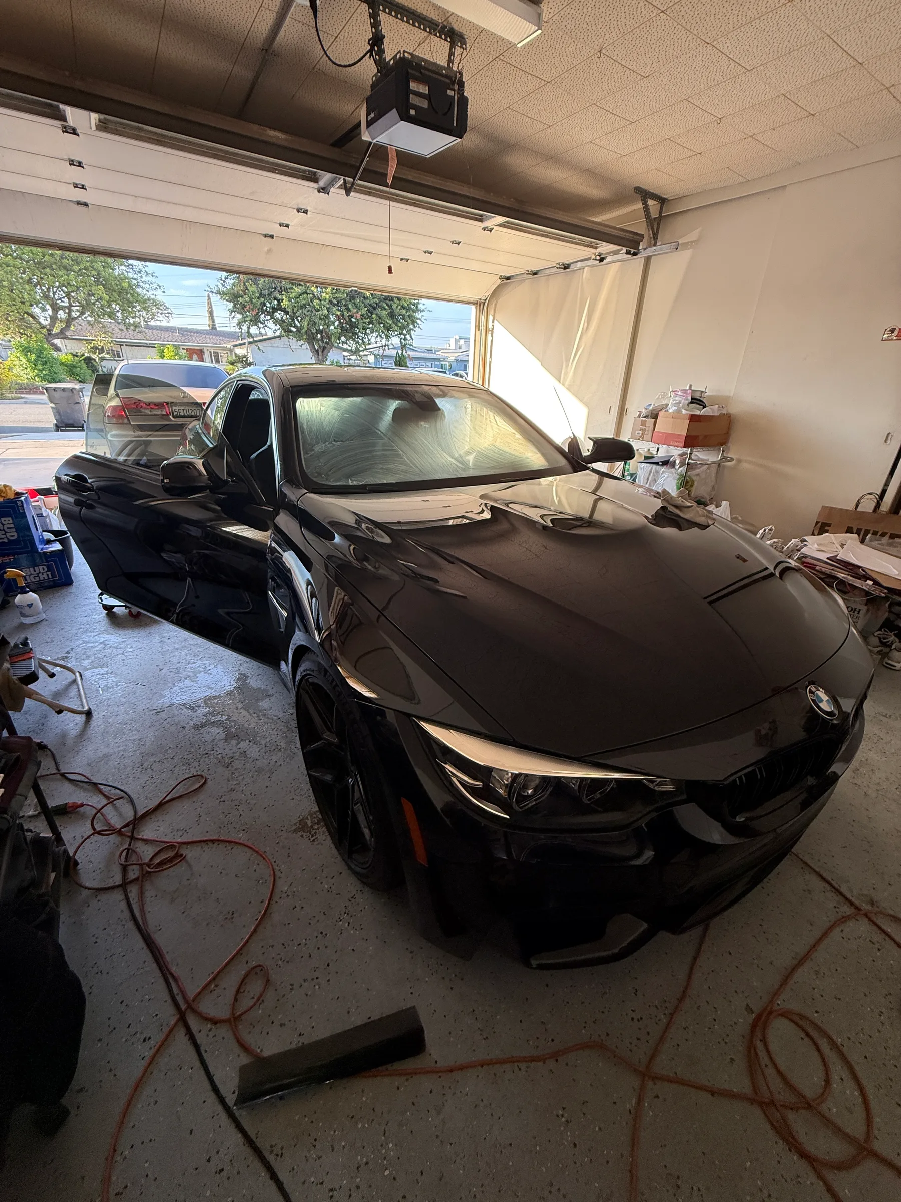 Black BMW sedan in a tint shop with the driver's door open, showing window tint application in progress.