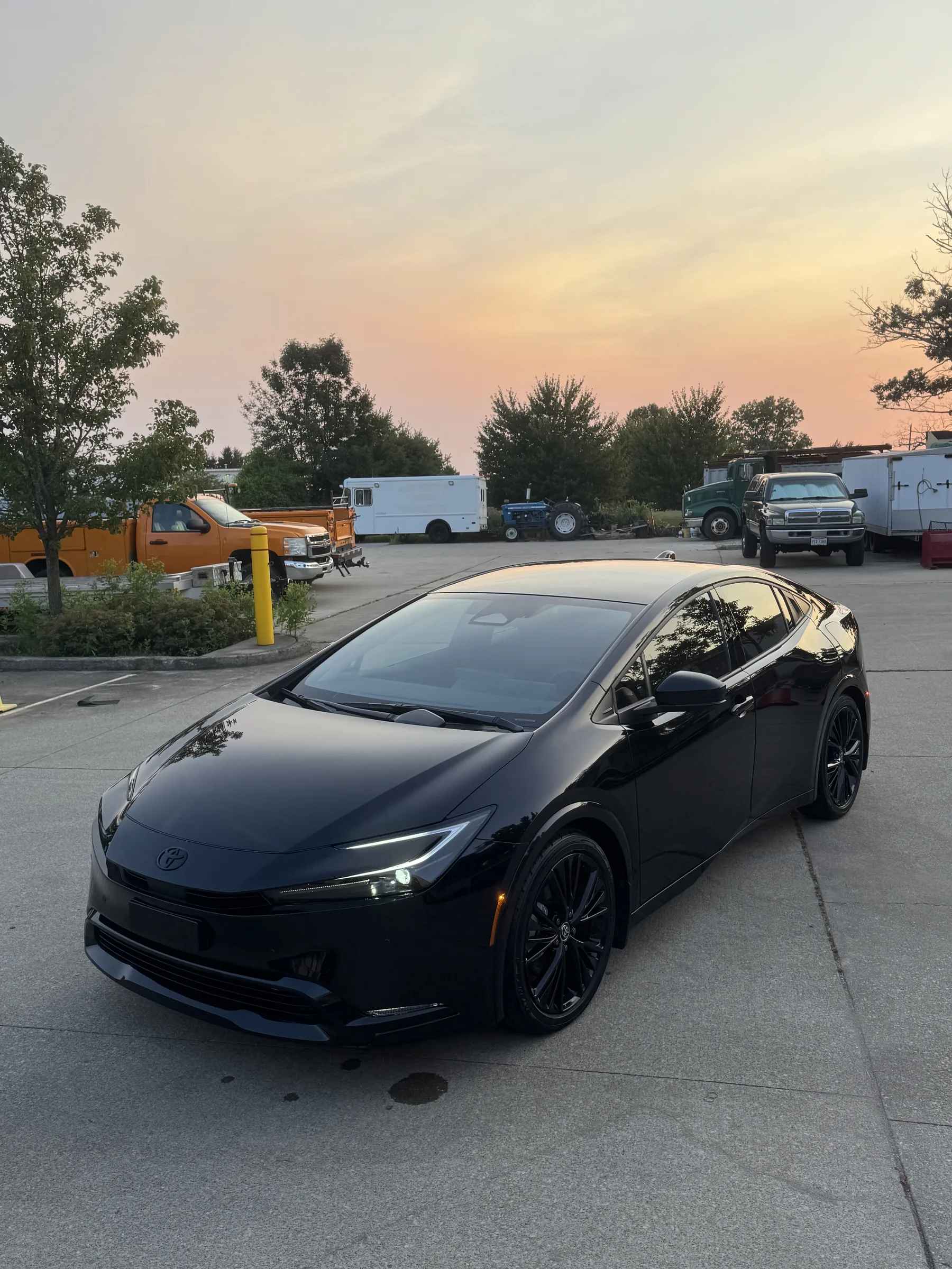 A black Toyota Prius with window tint parked in a commercial lot at sunset.