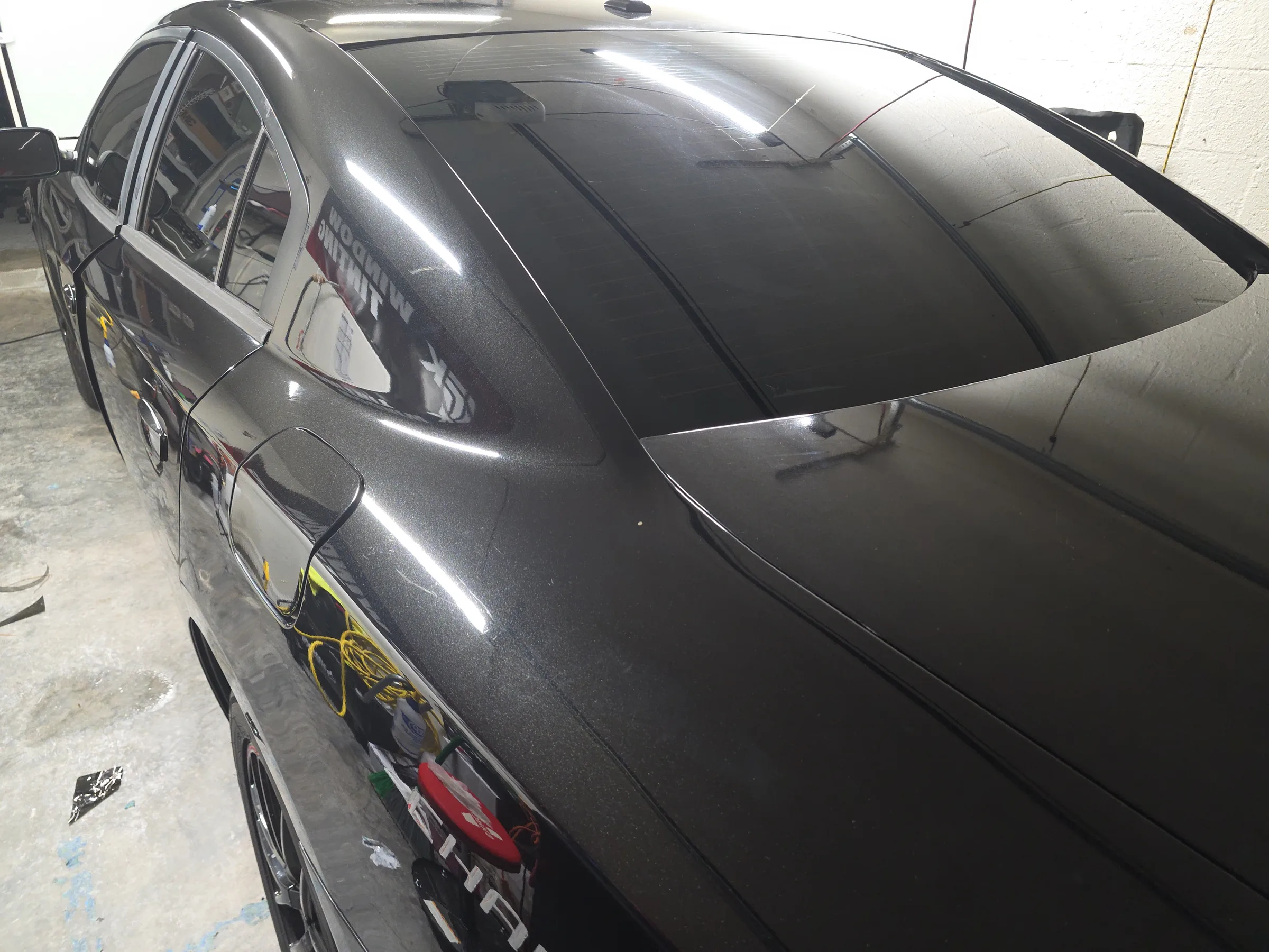 A gray sedan with dark window tint applied to the rear and side windows, parked in a shop bay.