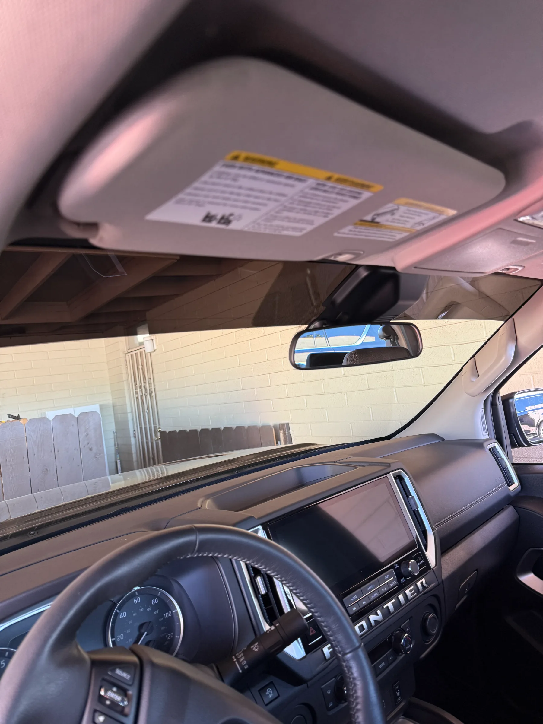 Interior view of a Nissan Frontier truck showing window tint film applied to the windshield with installation documentation visible on the sun visor.
