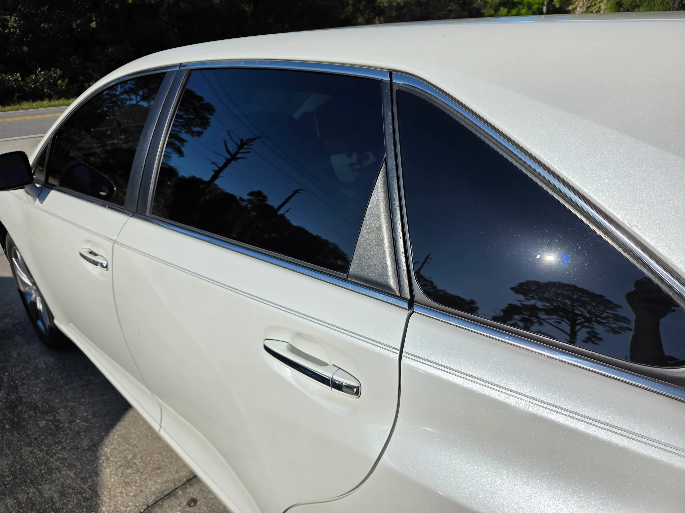 A white sedan with dark window tint applied to the rear and side windows, parked outdoors on a sunny day.