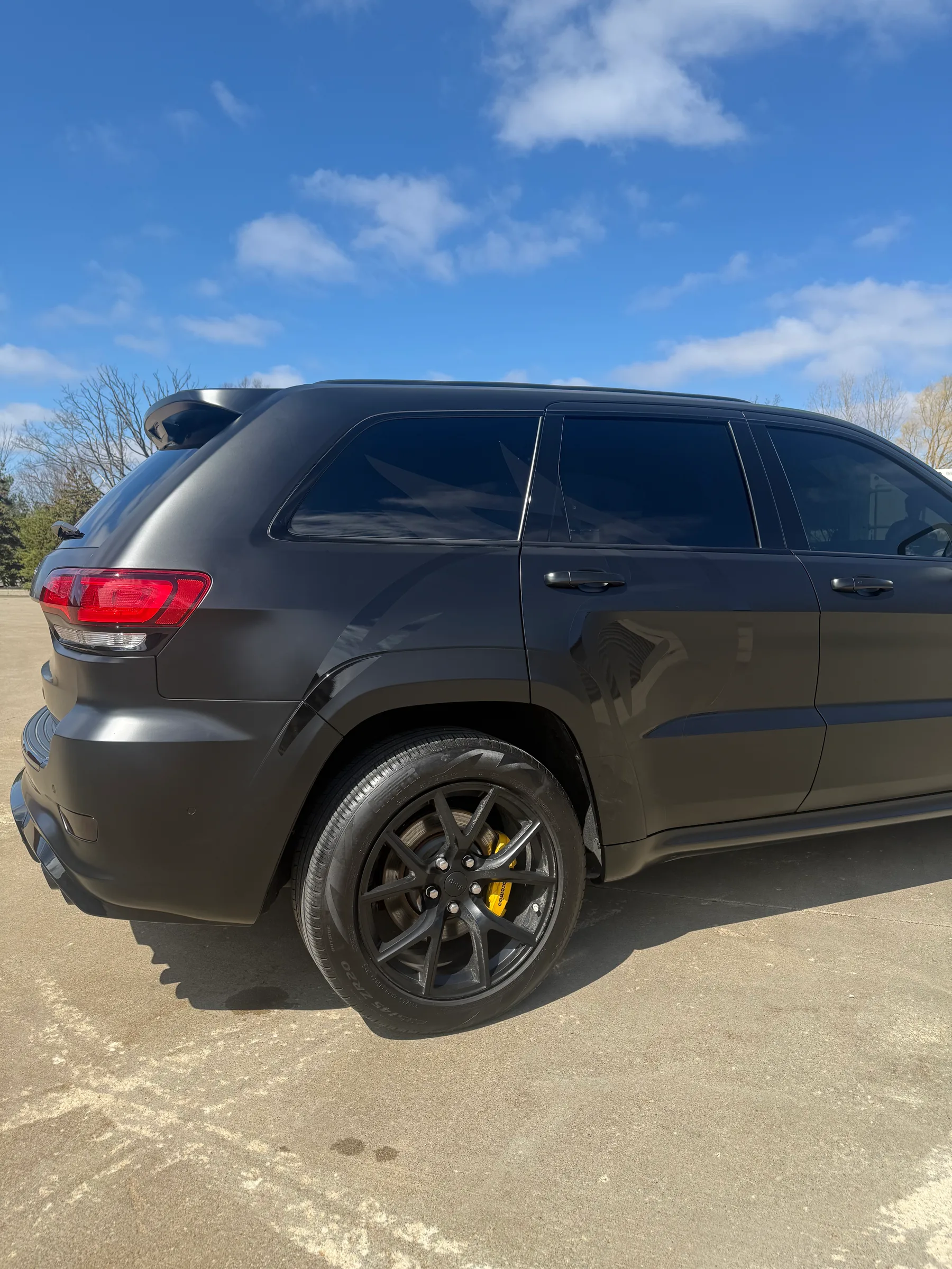 A black Jeep Grand Cherokee with dark window tint applied to all windows, shown from the rear three-quarter angle in daylight.