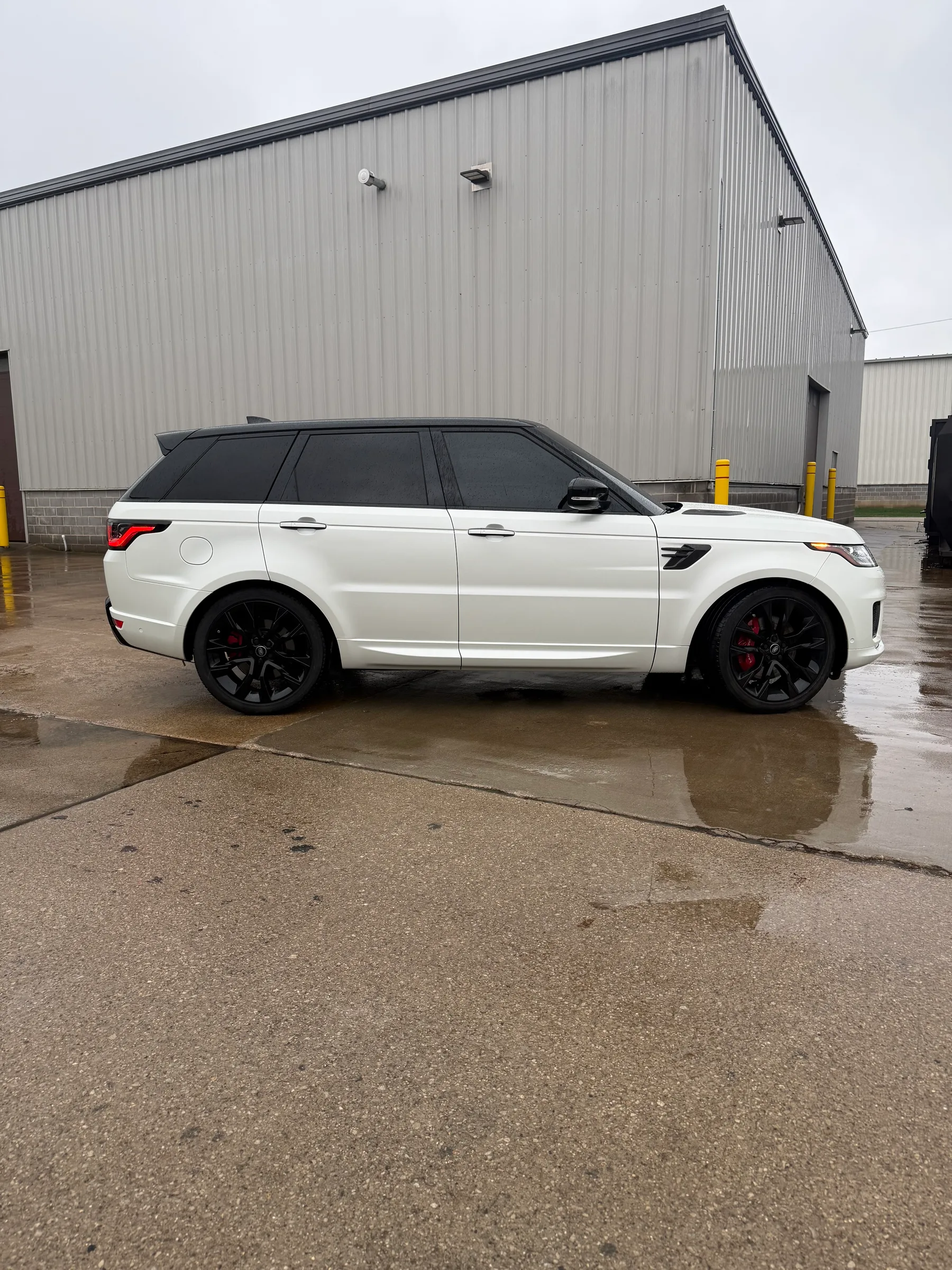 White Range Rover Sport with dark window tint parked in front of an industrial building.