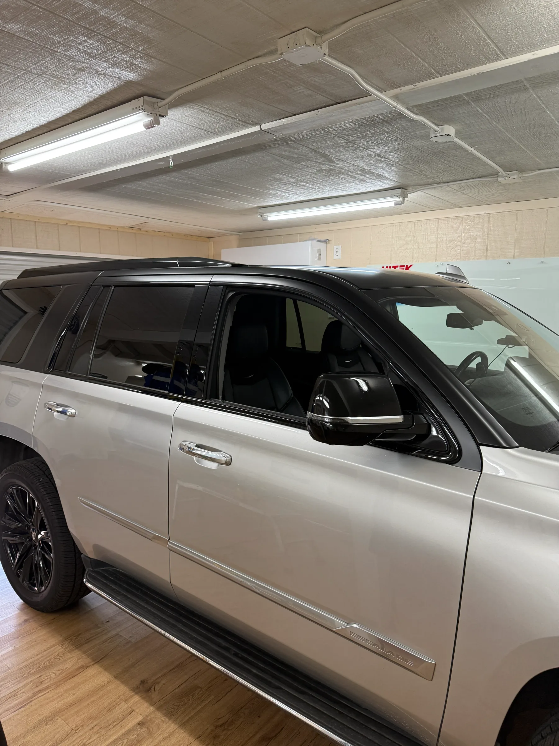 White SUV with dark window tint applied to all windows, parked indoors under fluorescent lights in a service bay.