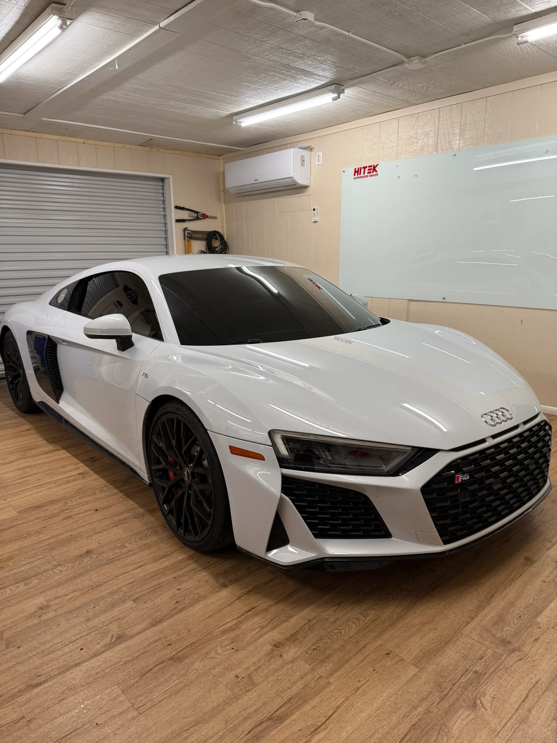 White Audi R8 sports car with dark window tint installed, displayed in a professional service bay.
