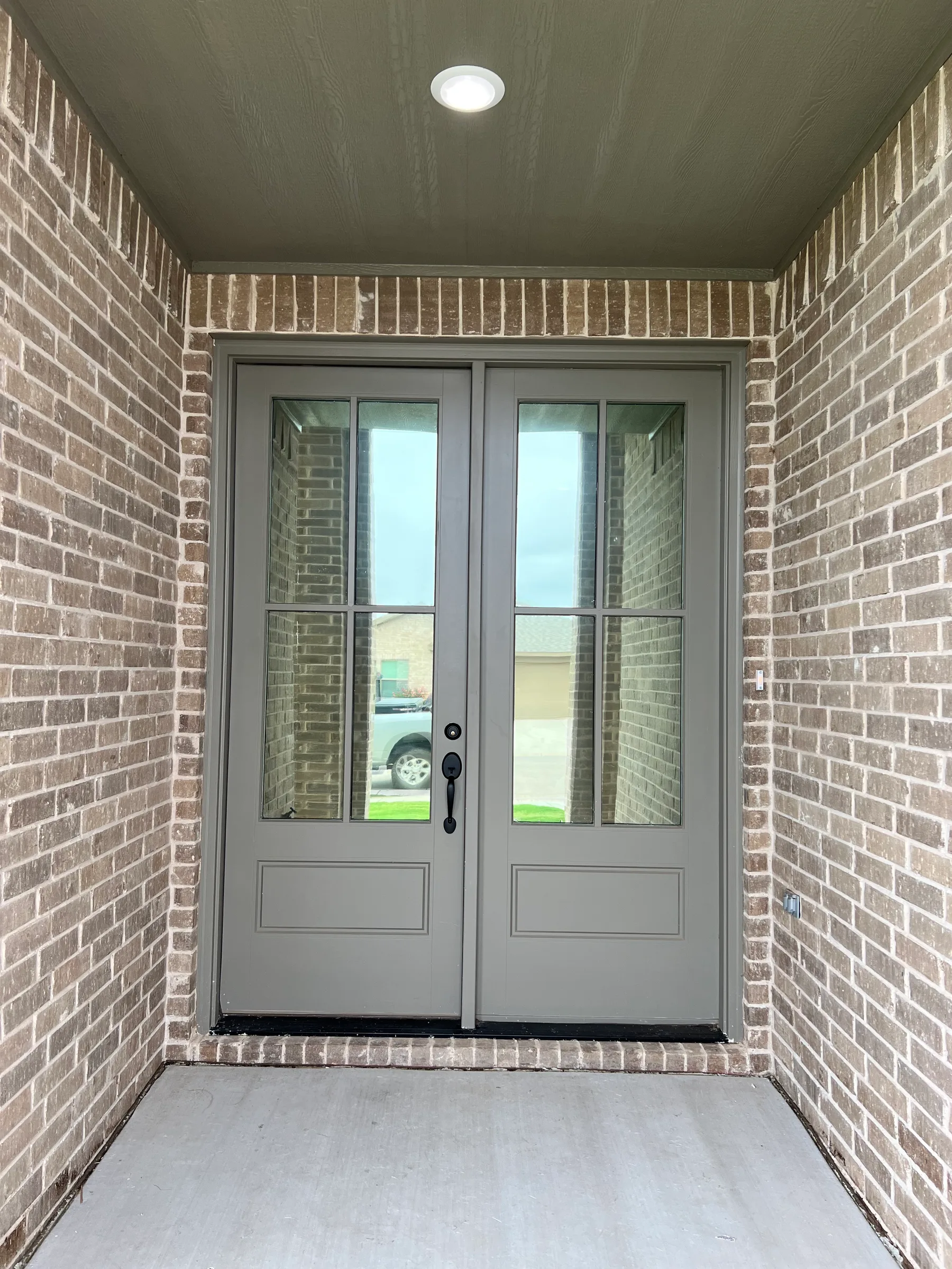 A residential front entrance with double glass doors framed by brick walls, showing clear glass panes with no window film applied.