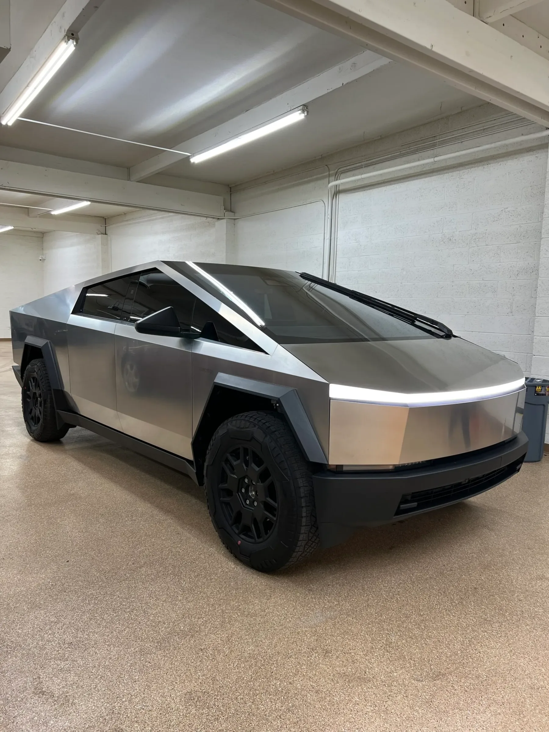 A Tesla Cybertruck with dark window tint applied to the side and rear windows, displayed in a professional indoor garage setting.