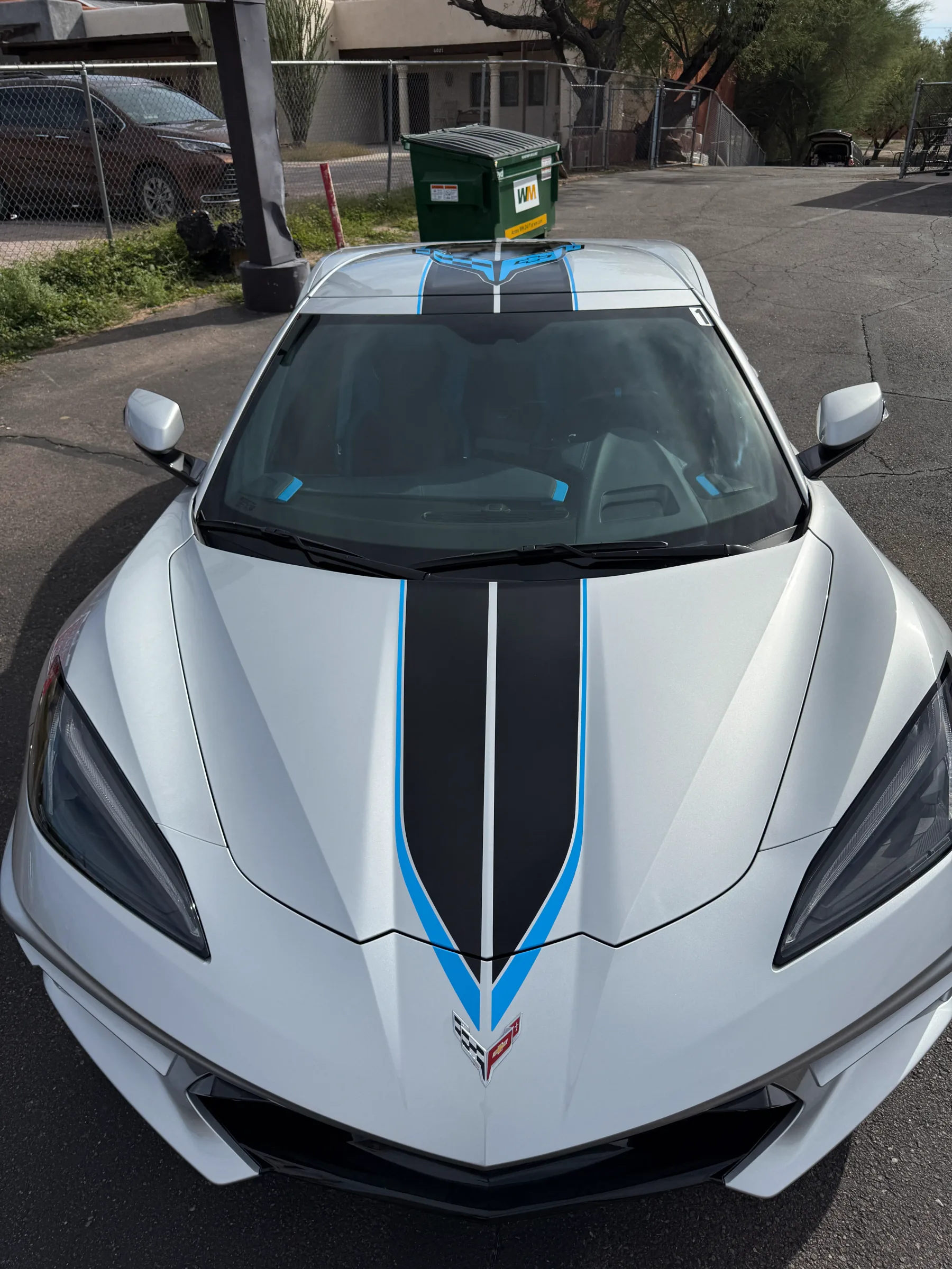 White Corvette sports car with black and blue racing stripe vinyl wrap applied to the hood and roof.