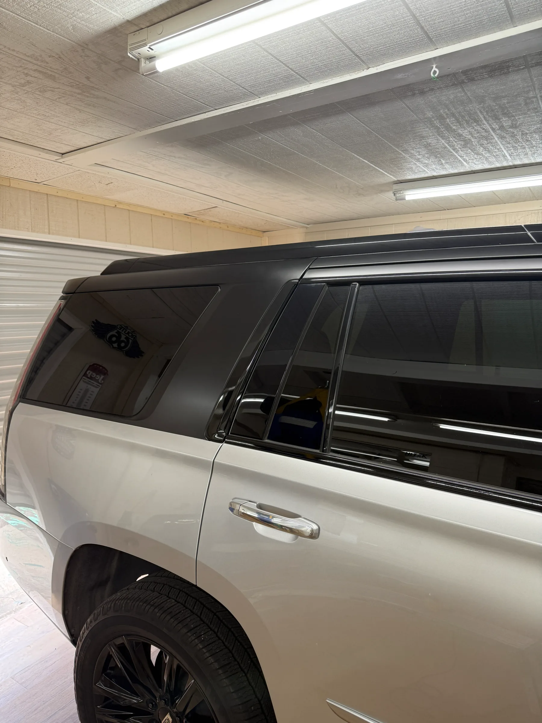 White SUV with dark window tint applied to all windows, parked indoors under bright shop lighting.