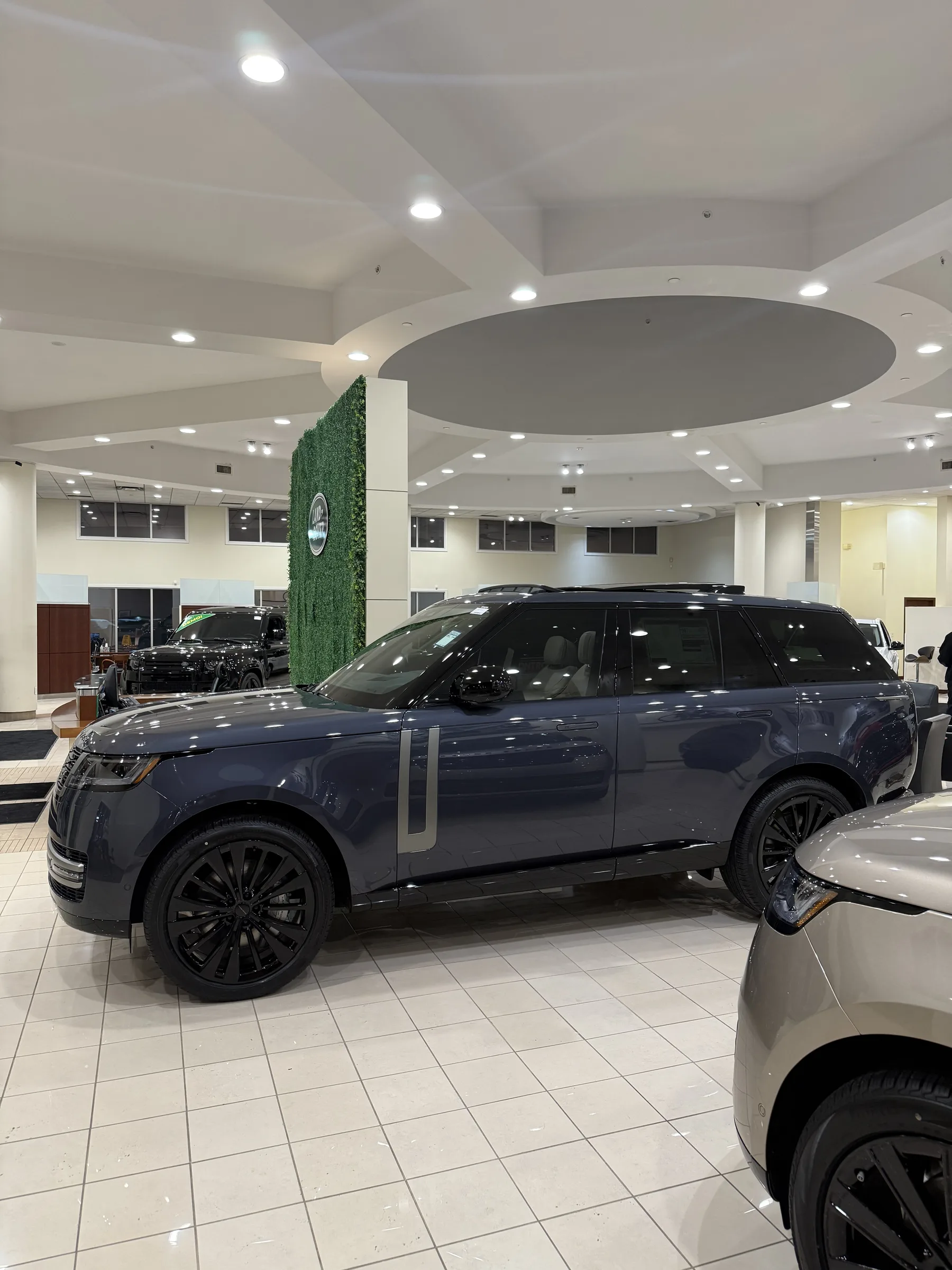 A dark blue Range Rover SUV displayed in a modern showroom interior with recessed lighting and a green branded accent wall.