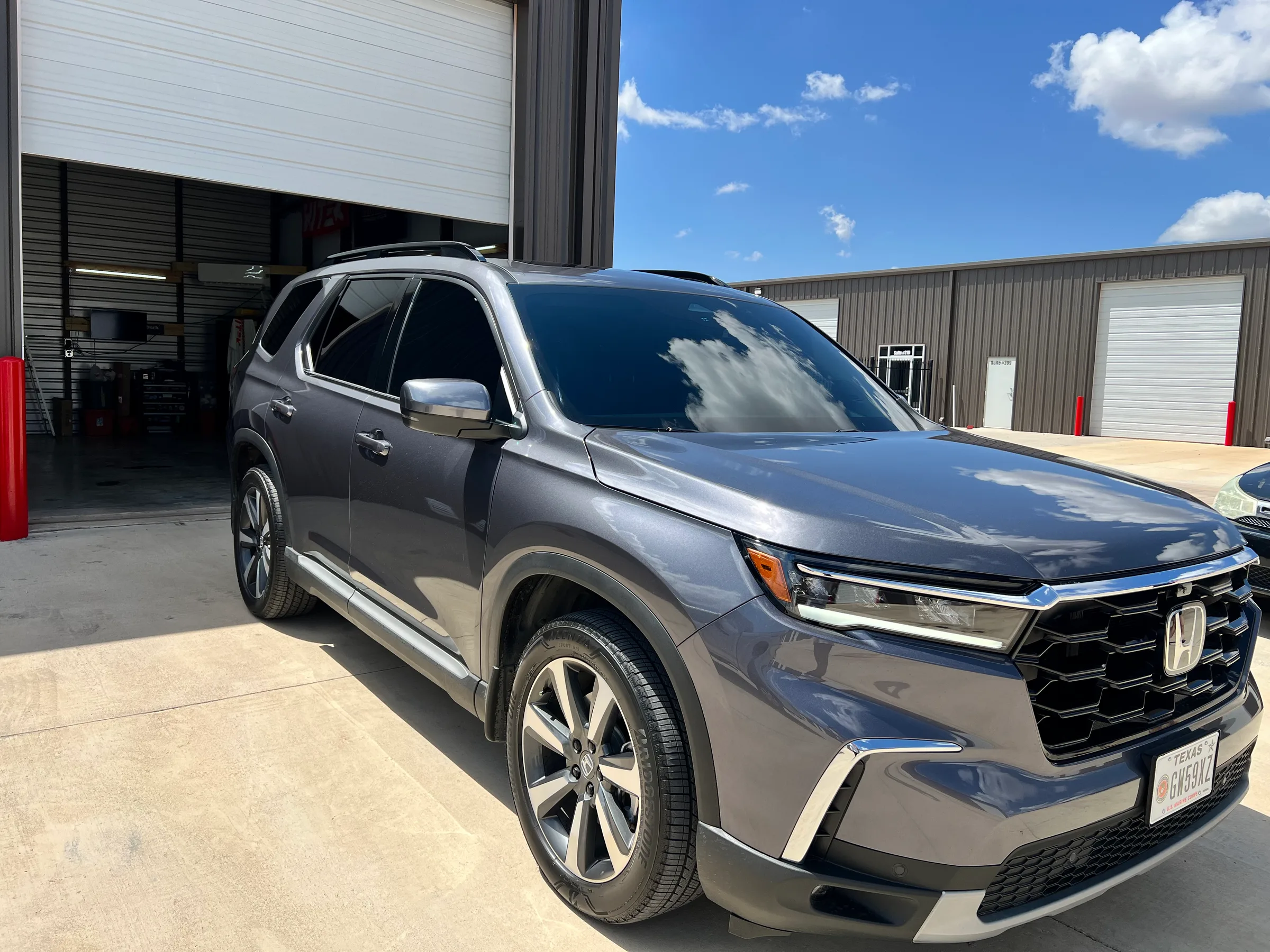 Gray Honda Pilot SUV with dark window tint applied, parked outside a service bay.