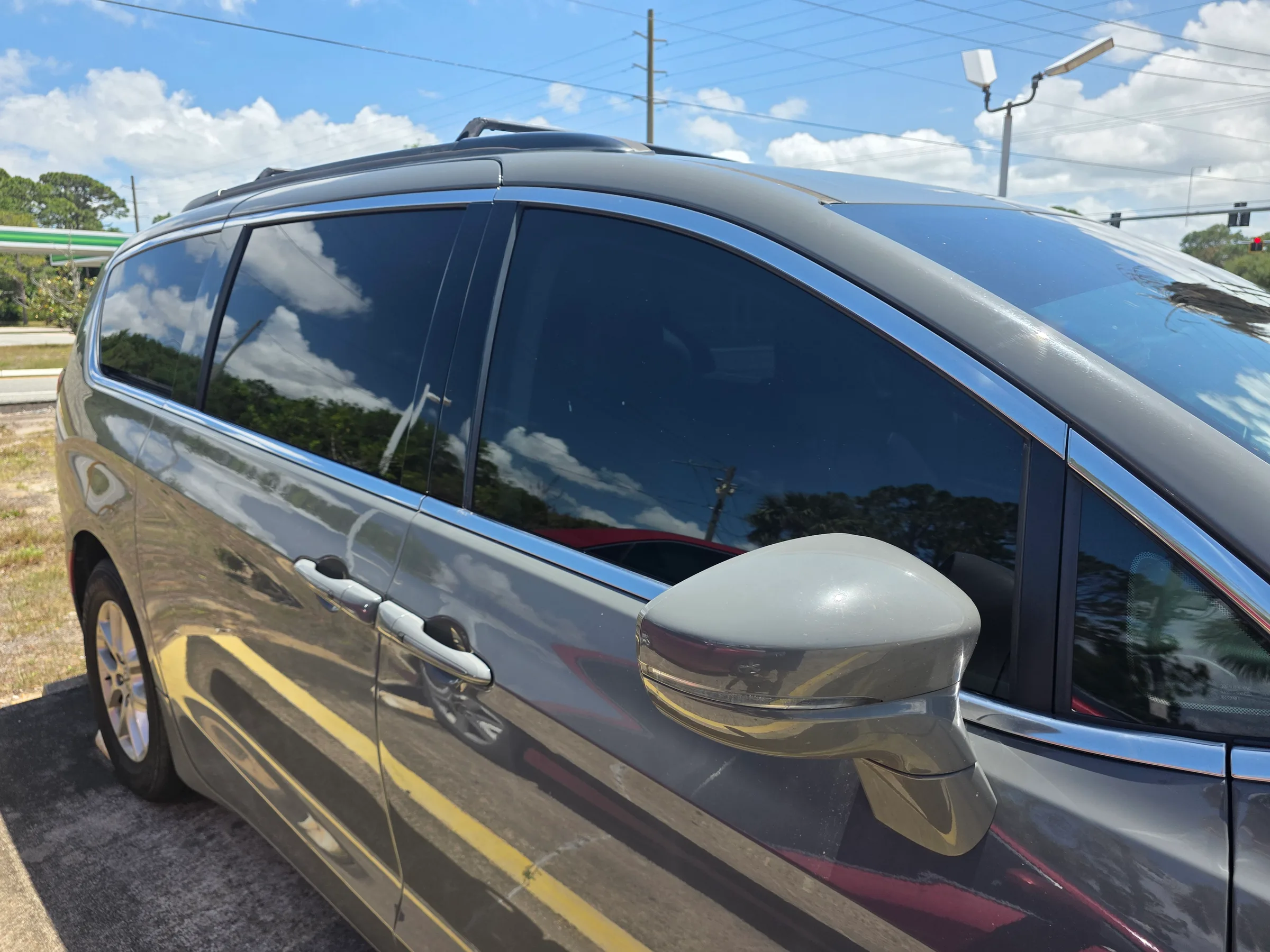 A gray minivan with dark window tint applied to all side and rear windows, parked in a lot.