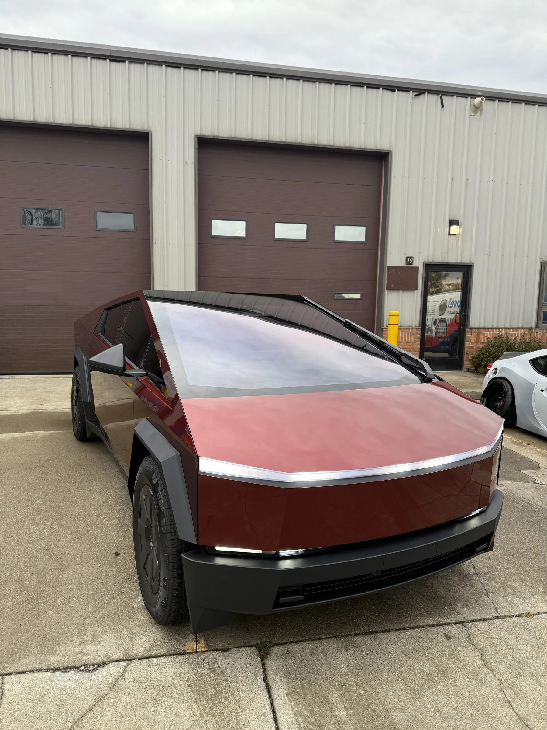 A Tesla Cybertruck with a two-tone red and white vinyl wrap parked outside an industrial shop in Berea, Ohio.