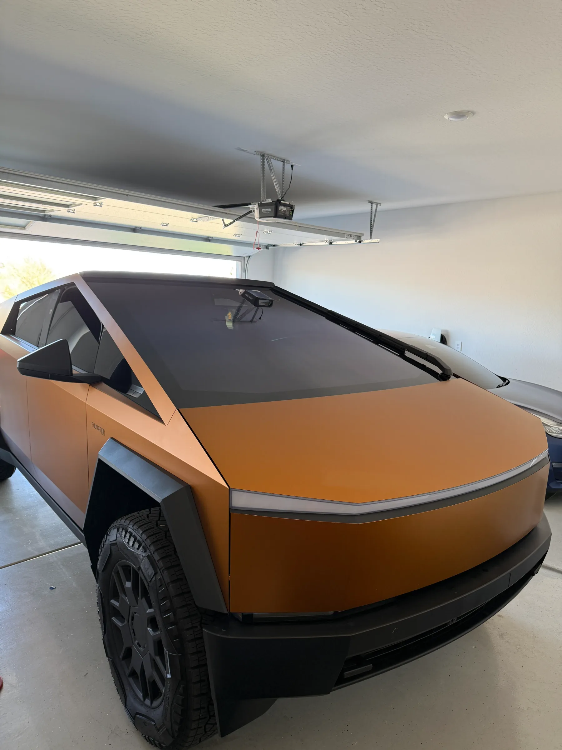 Orange Tesla Cybertruck with dark window tint applied, parked in an indoor garage bay.
