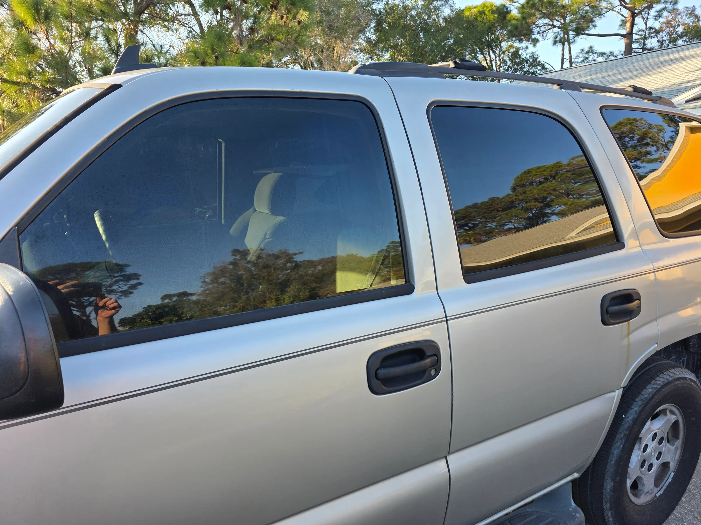 Silver minivan with dark window tint applied to the side windows, parked outdoors with trees in the background.