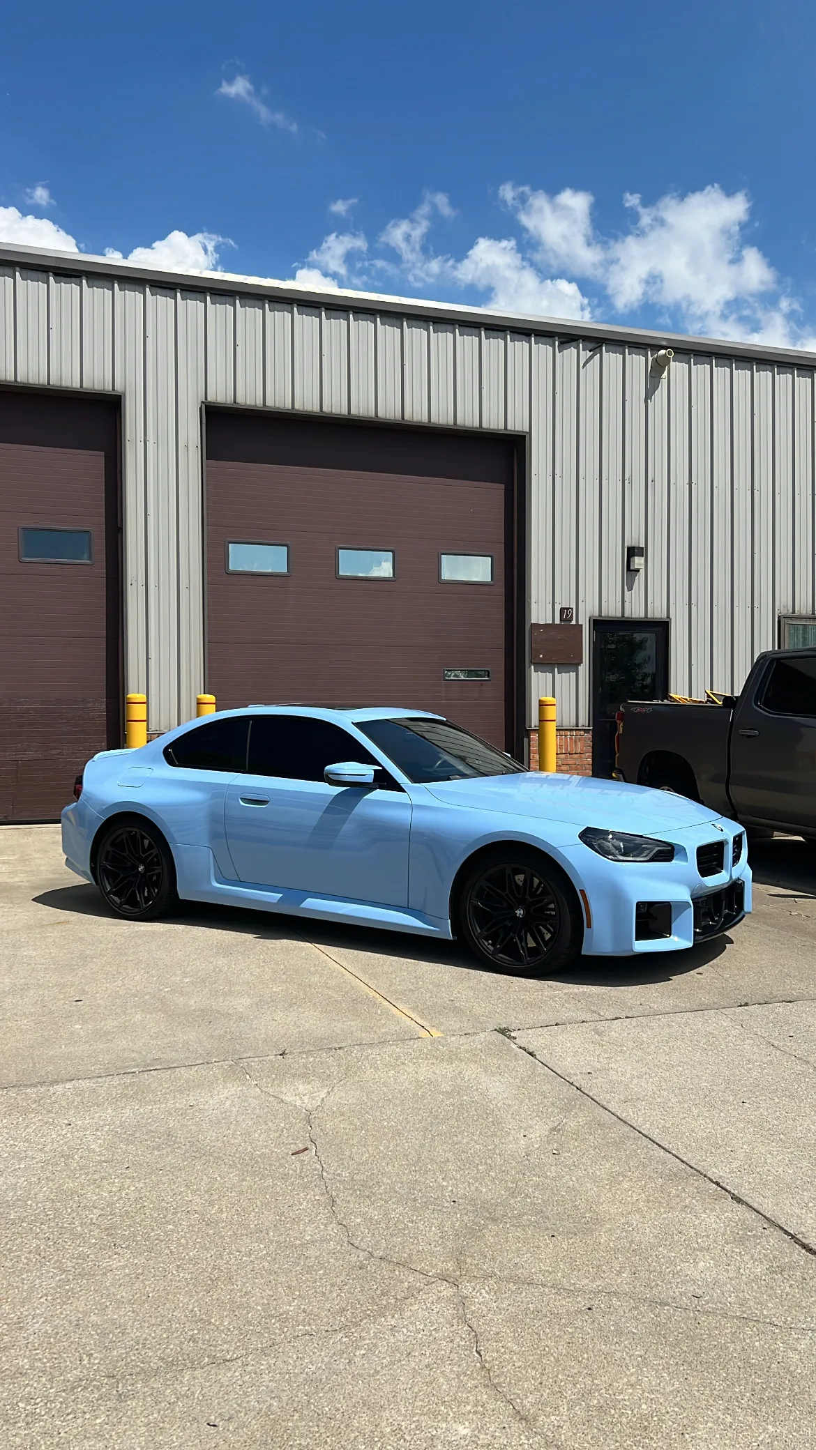 A light blue BMW M240i coupe with black wheels parked outside a commercial garage in Berea, Ohio.