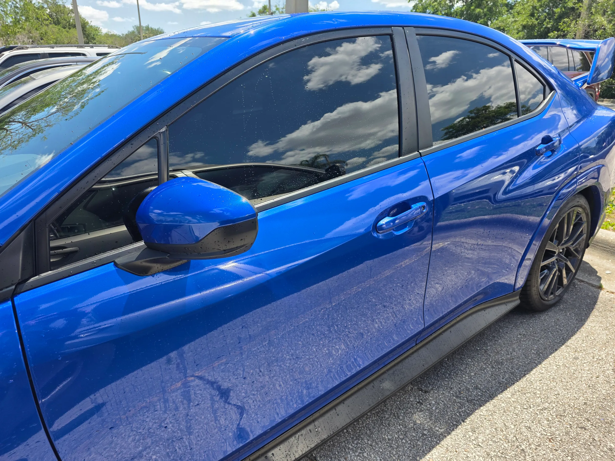 A bright blue sedan with dark window tint applied to the side windows, displayed in a parking lot.