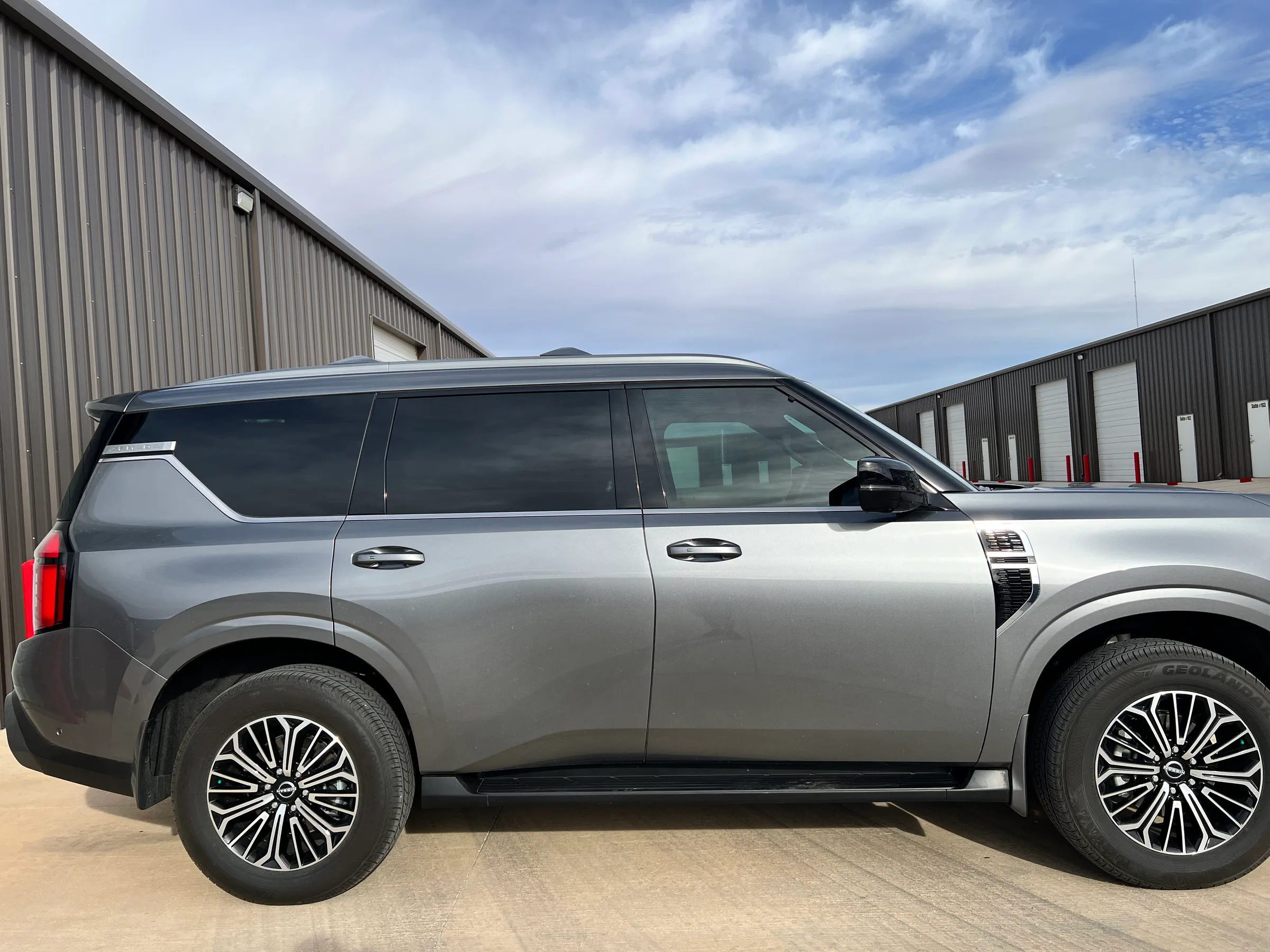 A gray Nissan Armada full-size SUV with dark window tinting applied, shown from the passenger side in front of an industrial building.